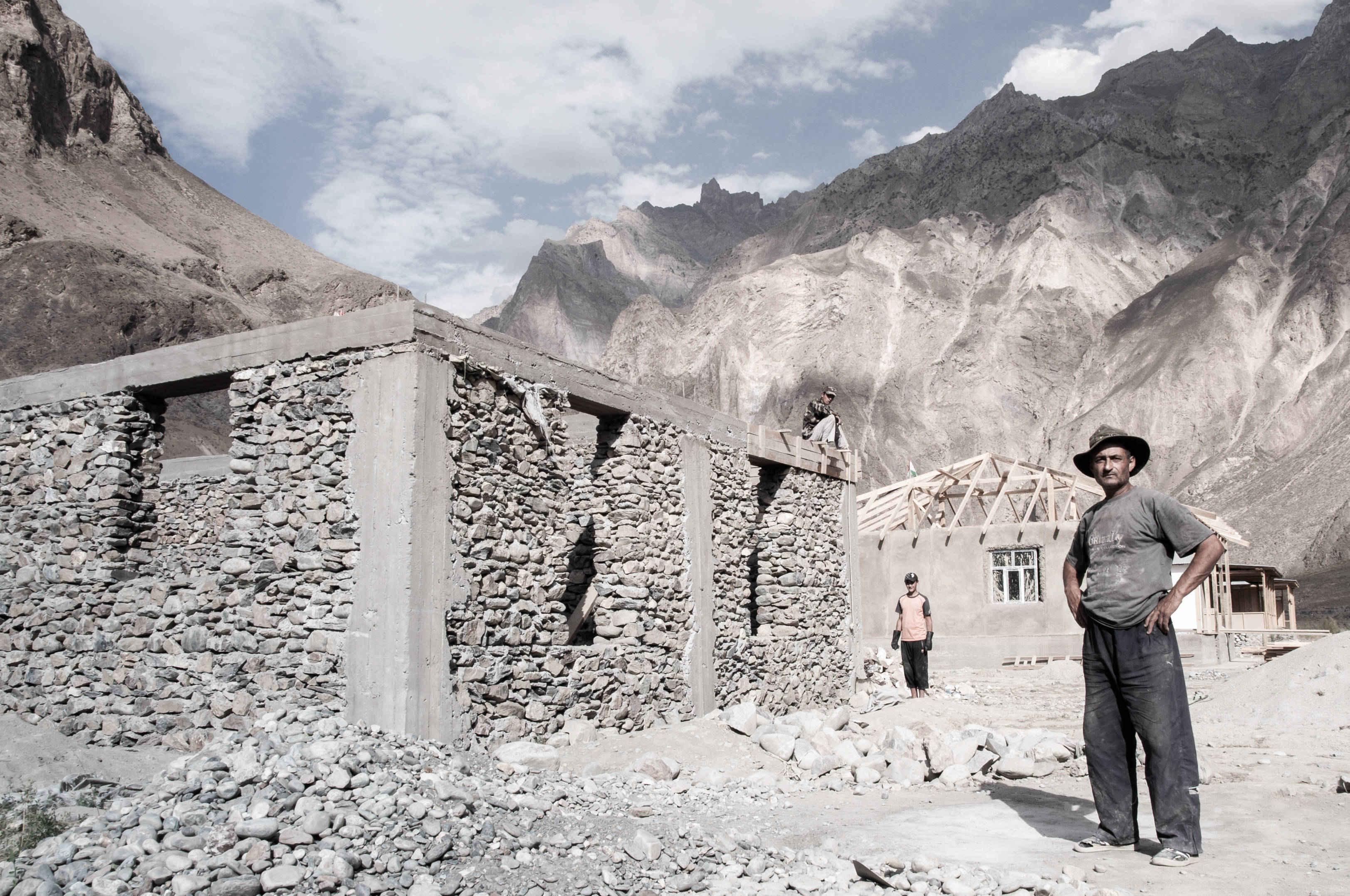 Tajikistan 桌布 壁紙 — 一個崎嶇的山村正在建設中，工人們在高聳的岩石山峰前建造石頭和混凝土結構。