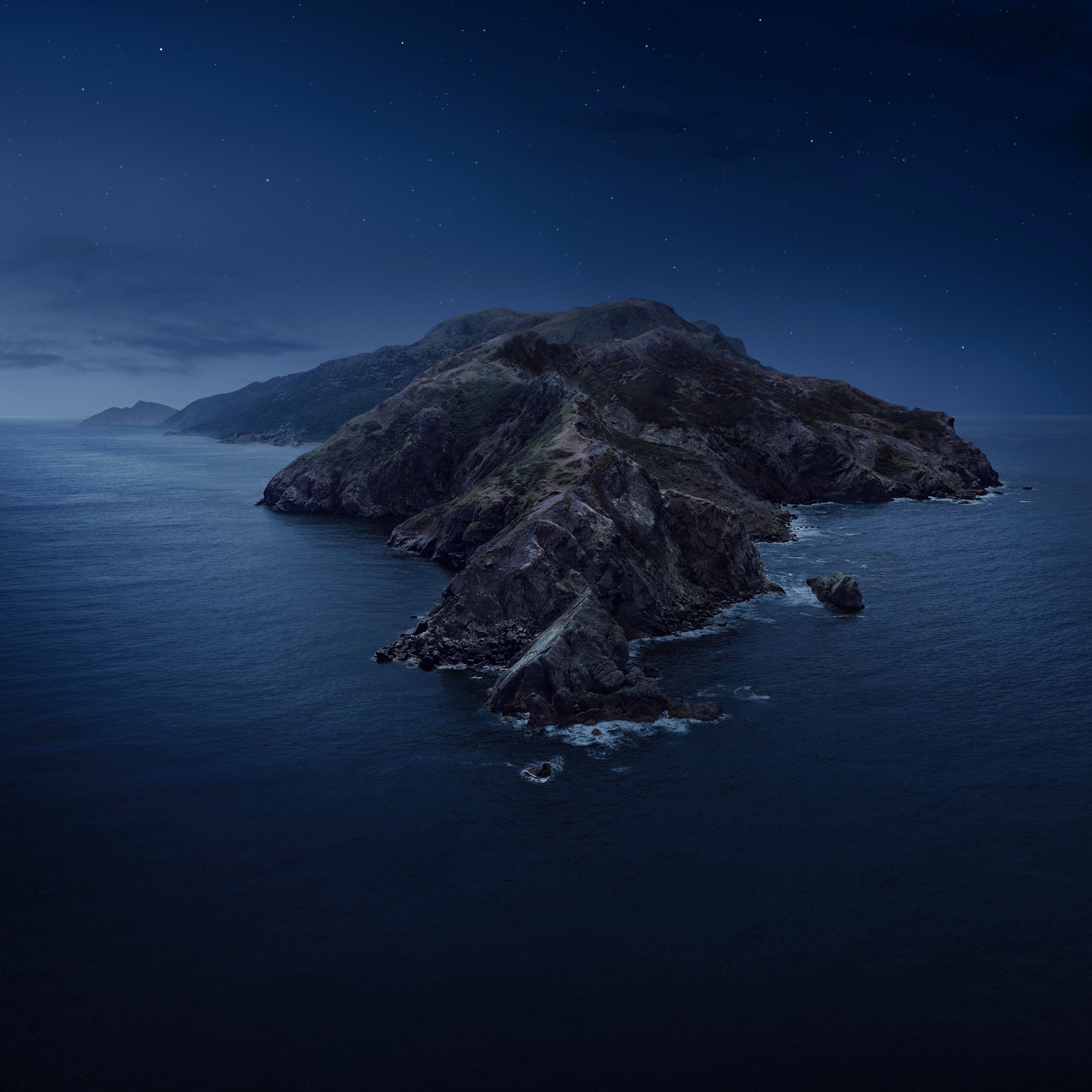 Catalina 桌布 壁紙 — 一個崎嶇的岩石島嶼從深藍色的海洋中升起，在繁星點點的夜空下，遠處有雲朵。