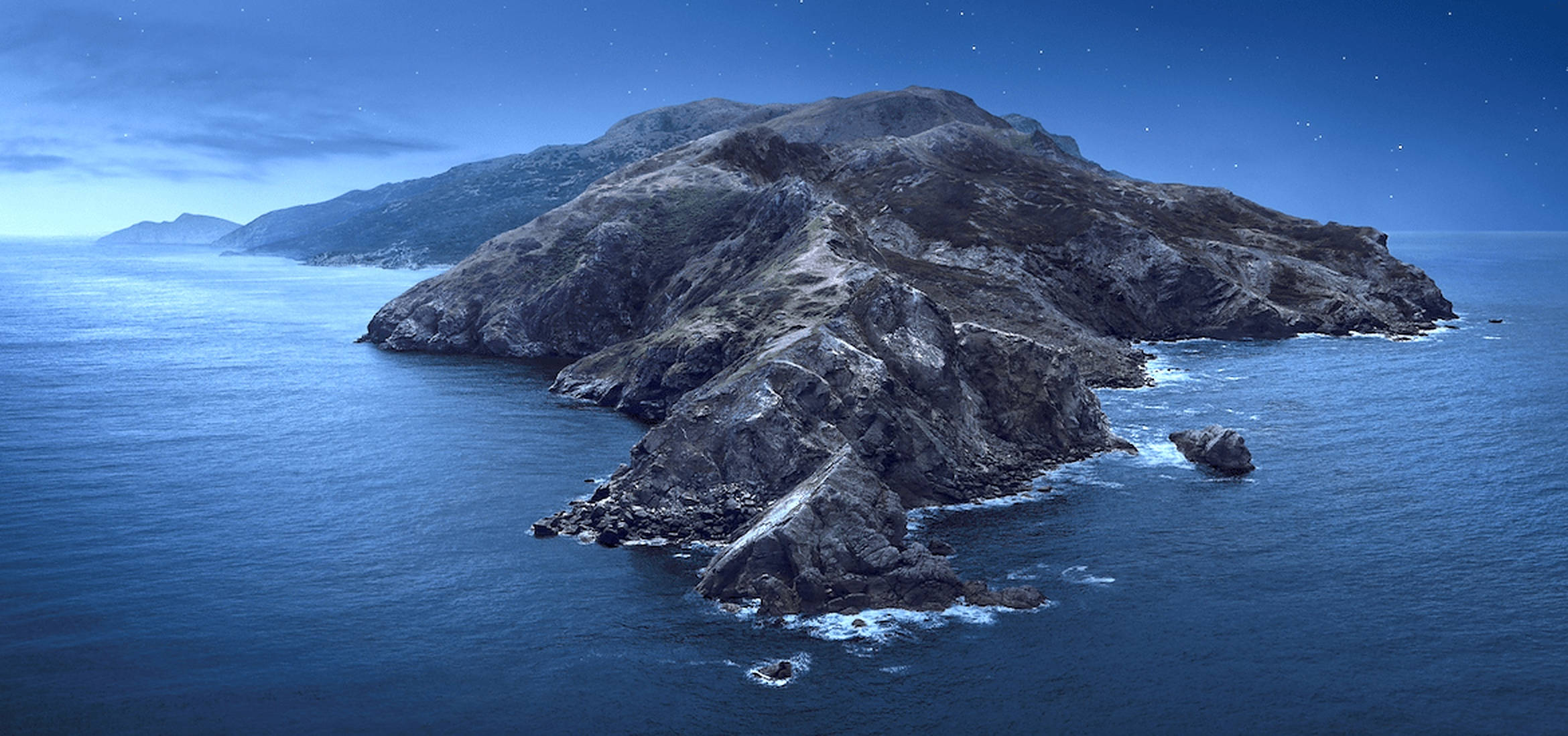 Catalina 桌布 壁紙 — 一個崎嶇的岩石島嶼從深藍色的海洋中升起，在繁星點點的夜空下，地平線上有遙遠的山脈。