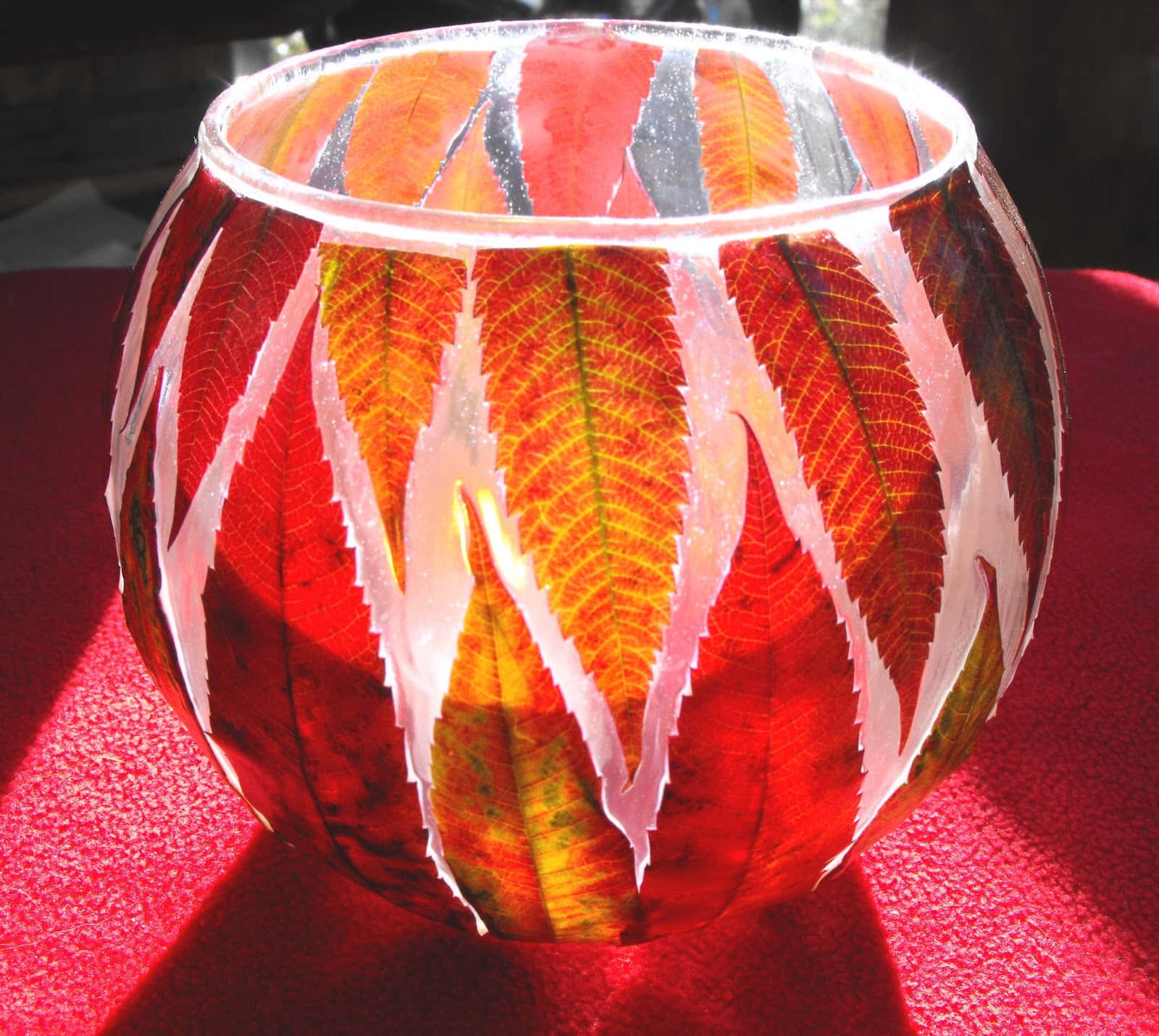 Fall Crafts 桌布 壁紙 — 一個嵌有鮮豔紅色、橙色和黃色秋葉的玻璃碗，在紅色紋理表面上投射出彩色光線。