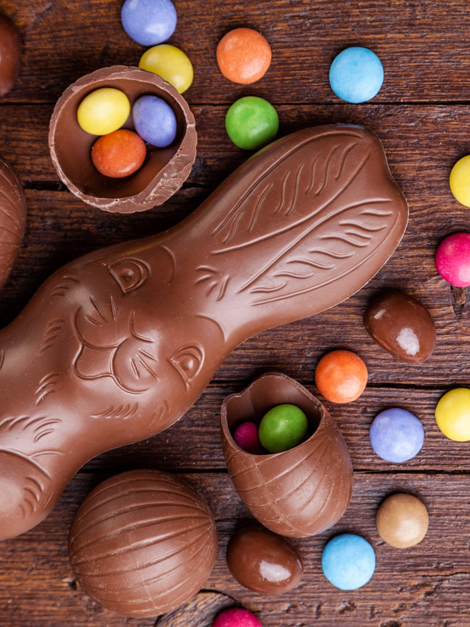 Easter Phone 桌布 壁紙 — 一個巧克力復活節兔子和裝滿彩色糖果的雞蛋放在質樸的木質表面上。