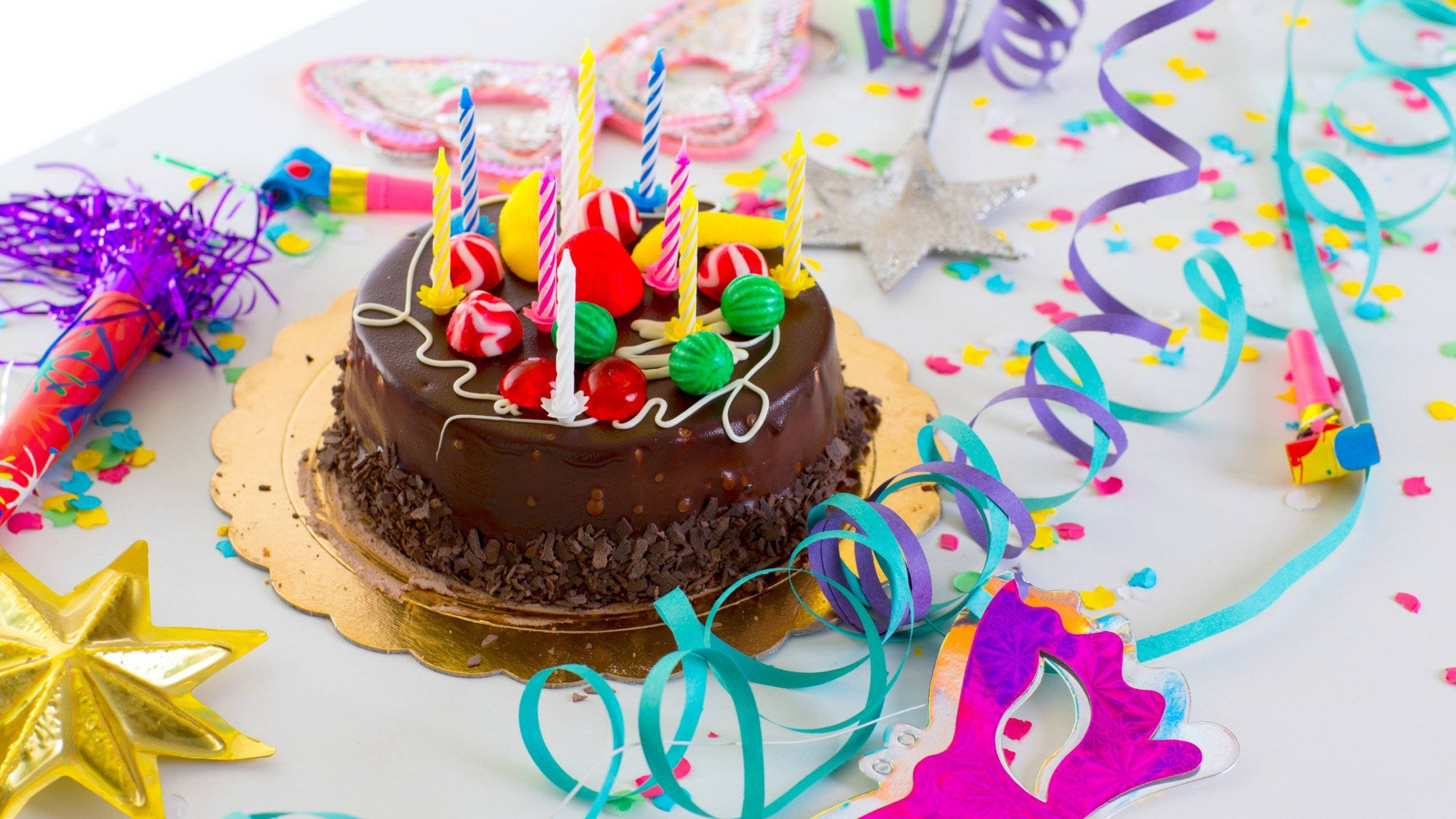 Birthday Cake 桌布 壁紙 — 一個巧克力生日蛋糕，上面有彩色糖果和蠟燭，周圍是派對五彩紙屑彩帶和裝飾。