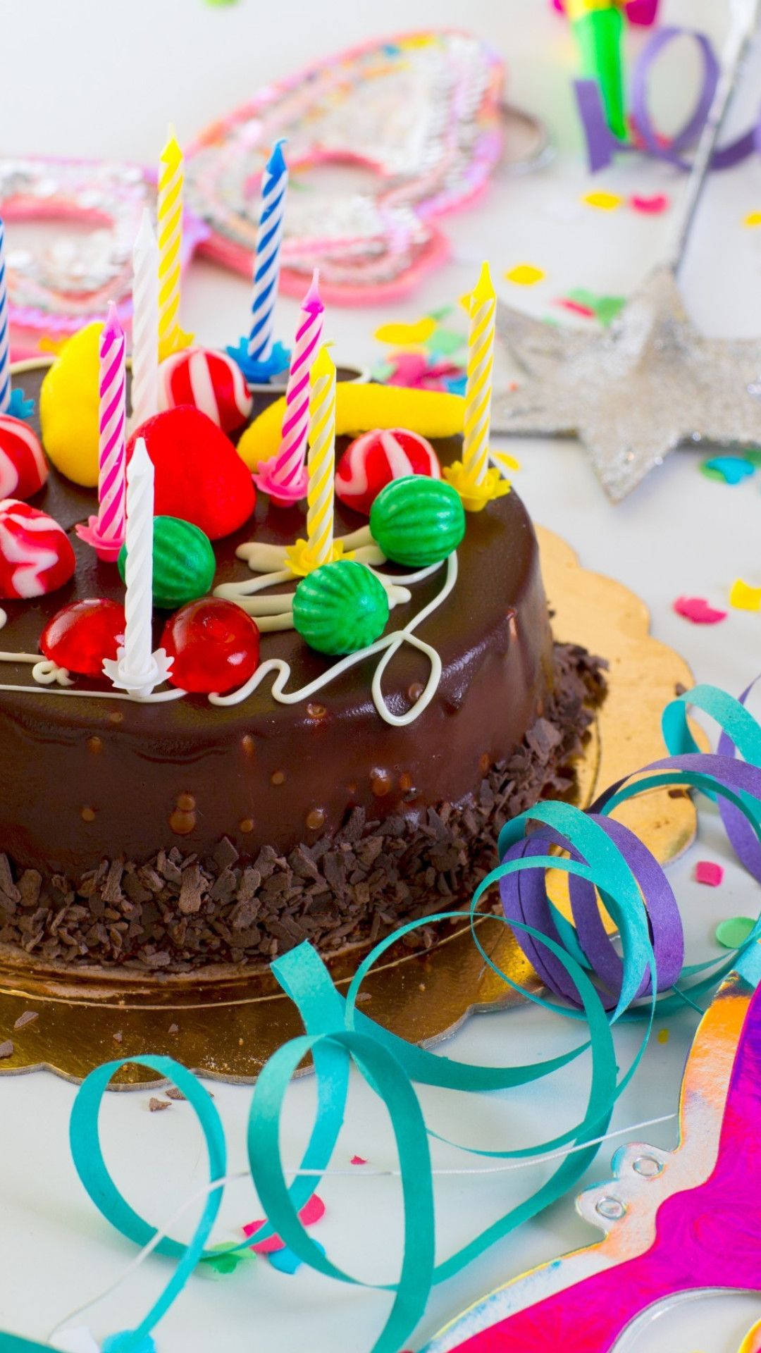 生日快樂 桌布 壁紙 — 一個巧克力生日蛋糕，上面有彩色蠟燭和糖果，周圍是派對裝飾。