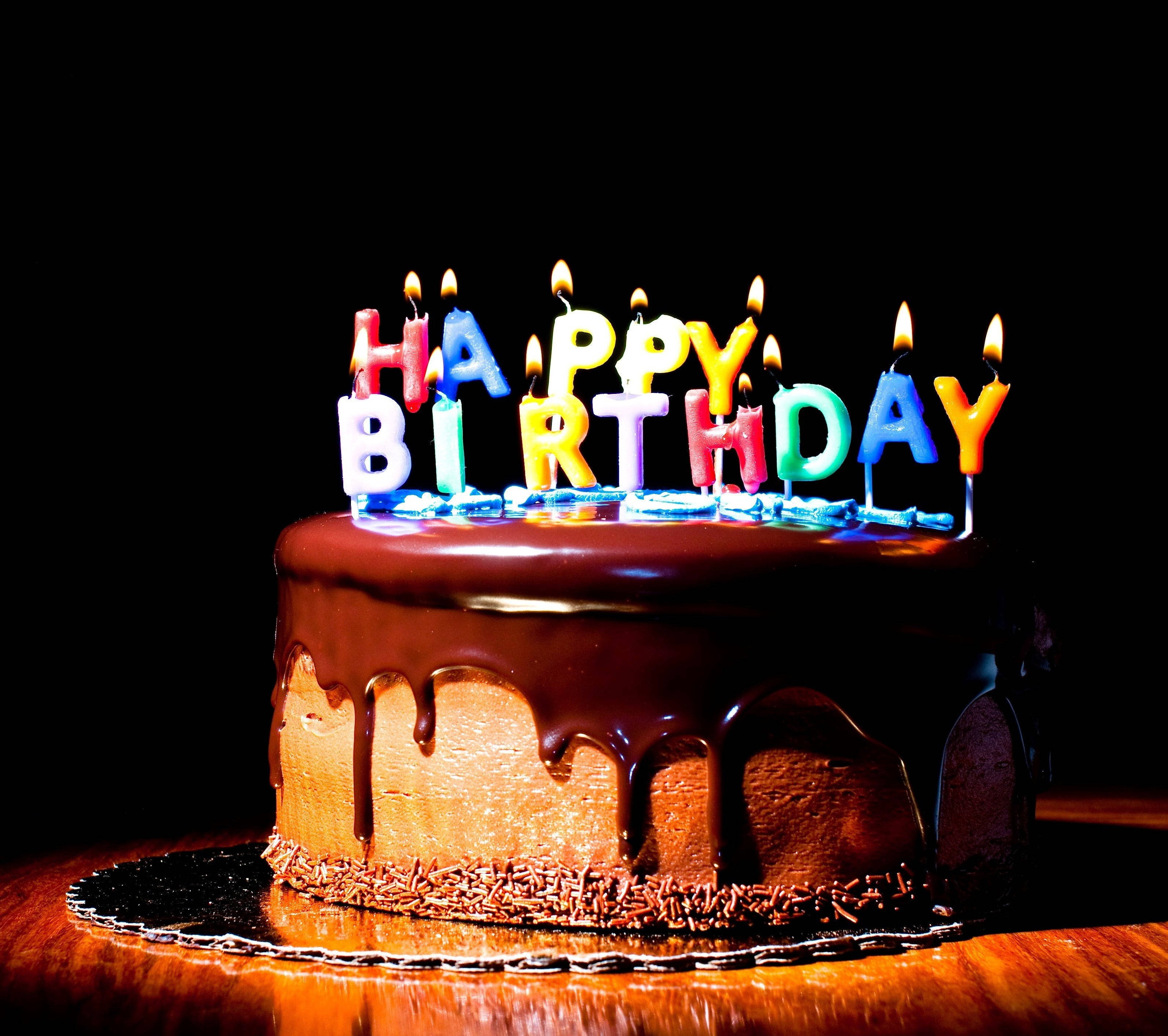 Birthday 桌布 壁紙 — 一個巧克力生日蛋糕，上面有滴落的糖霜和色彩繽紛的點燃蠟燭，在黑色背景上拼出生日快樂。