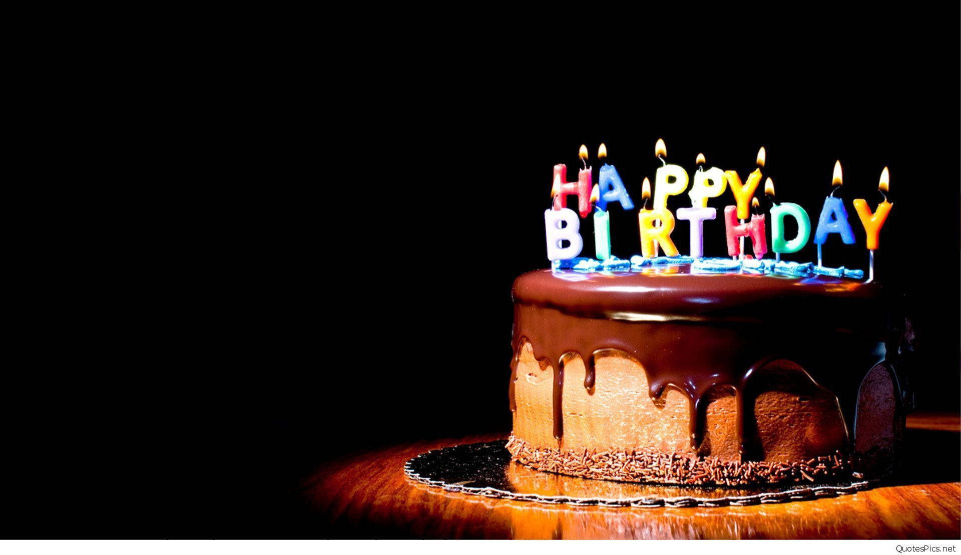 生日快樂 桌布 壁紙 — 一個巧克力生日蛋糕，帶有滴落的糖霜和拼出 happy birthday 的彩色蠟燭，在黑色背景上發光。