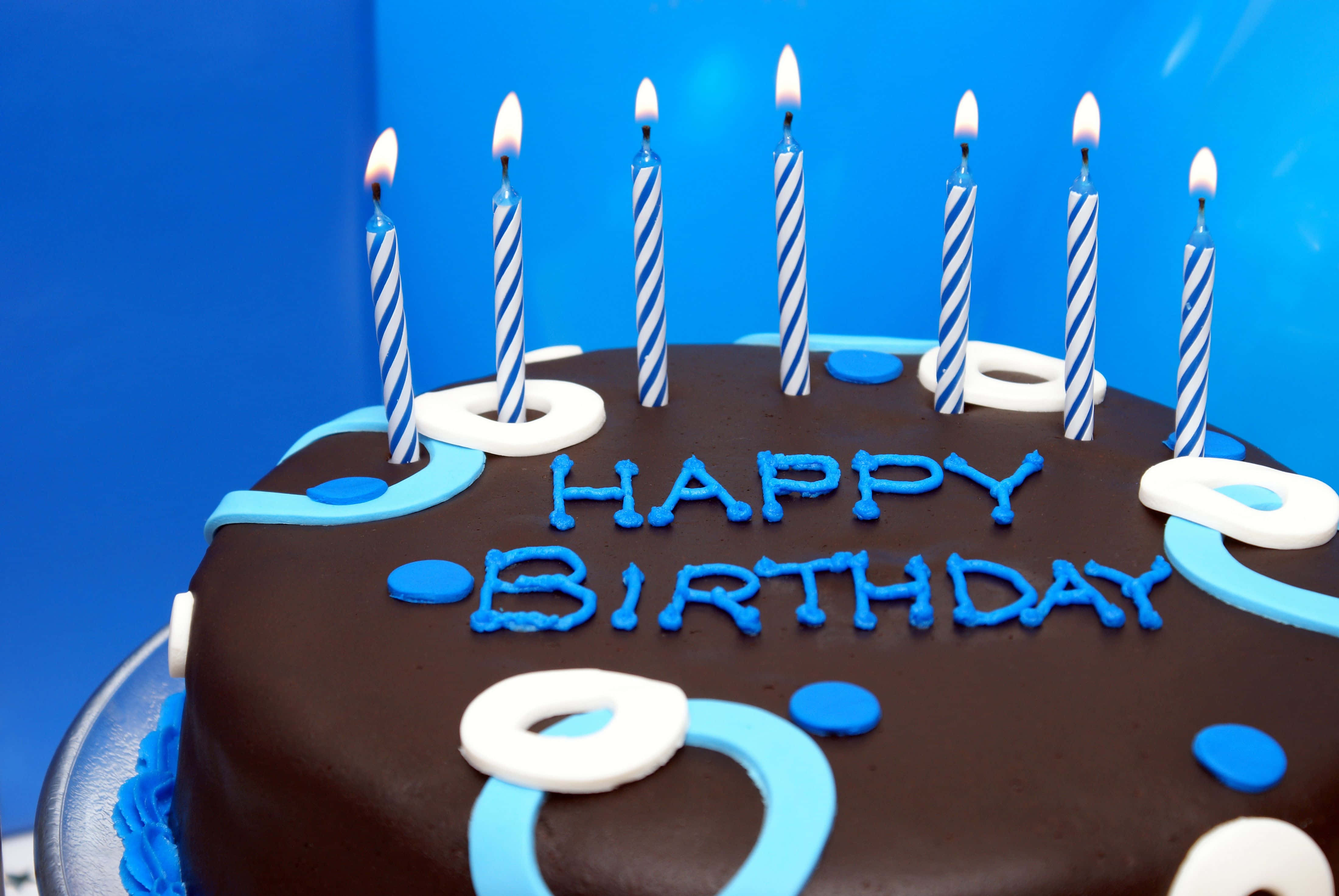 生日快樂 桌布 壁紙 — 一個巧克力生日蛋糕，帶有藍色和白色蠟燭，以及「HAPPY BIRTHDAY」糖霜，襯托在充滿活力的藍色背景上。