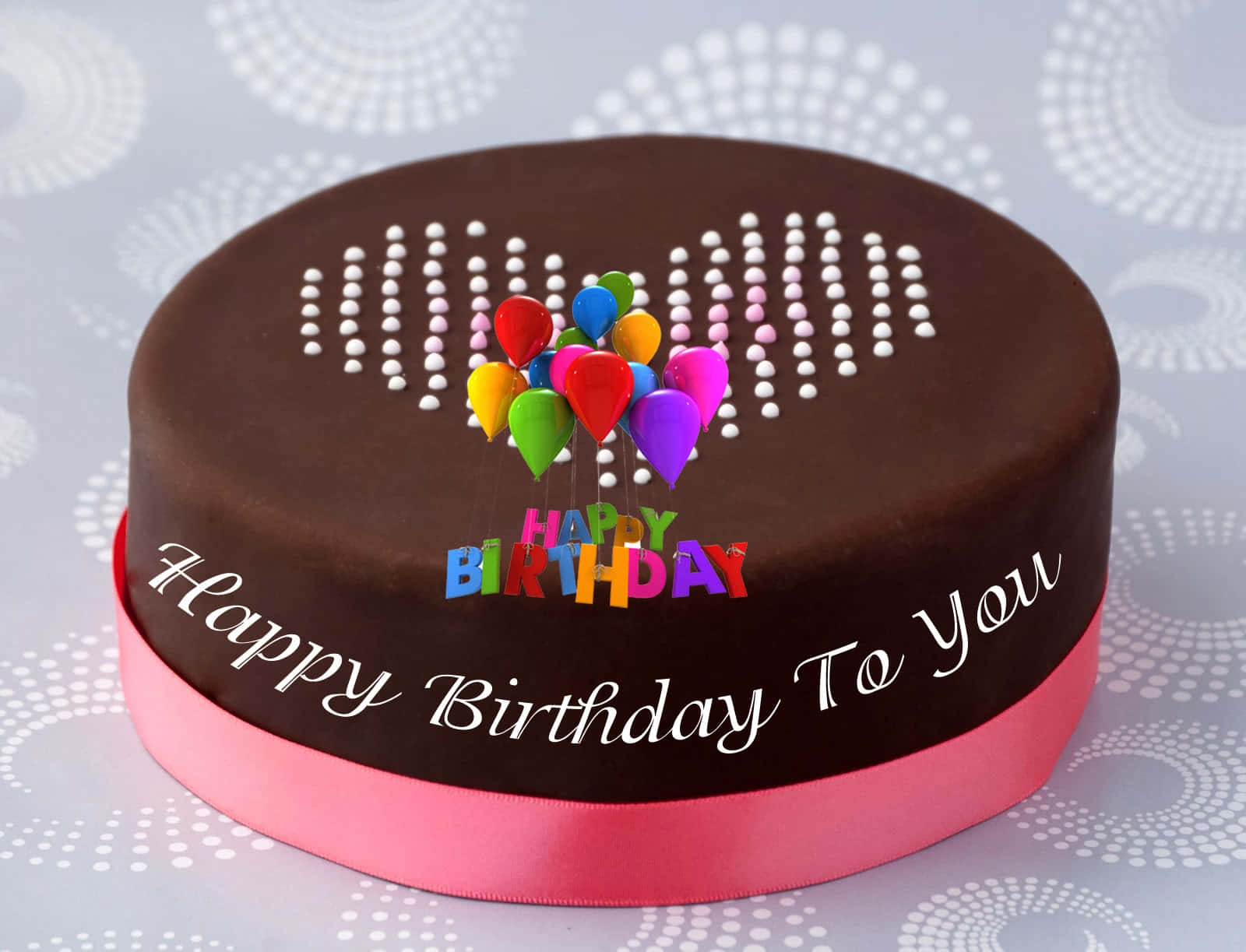 Birthday Cakes 桌布 壁紙 — 一個巧克力生日蛋糕，裝飾著彩色氣球和粉紅色絲帶，放在有圖案的表面上。