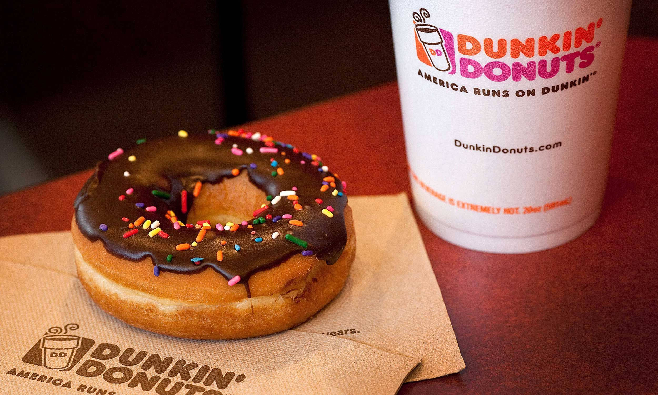 donuts 桌布 壁紙 — 一個巧克力糖霜甜甜圈配上彩色糖粒，放在有品牌標誌的餐巾紙上，旁邊有一杯Dunkin' Donuts咖啡。