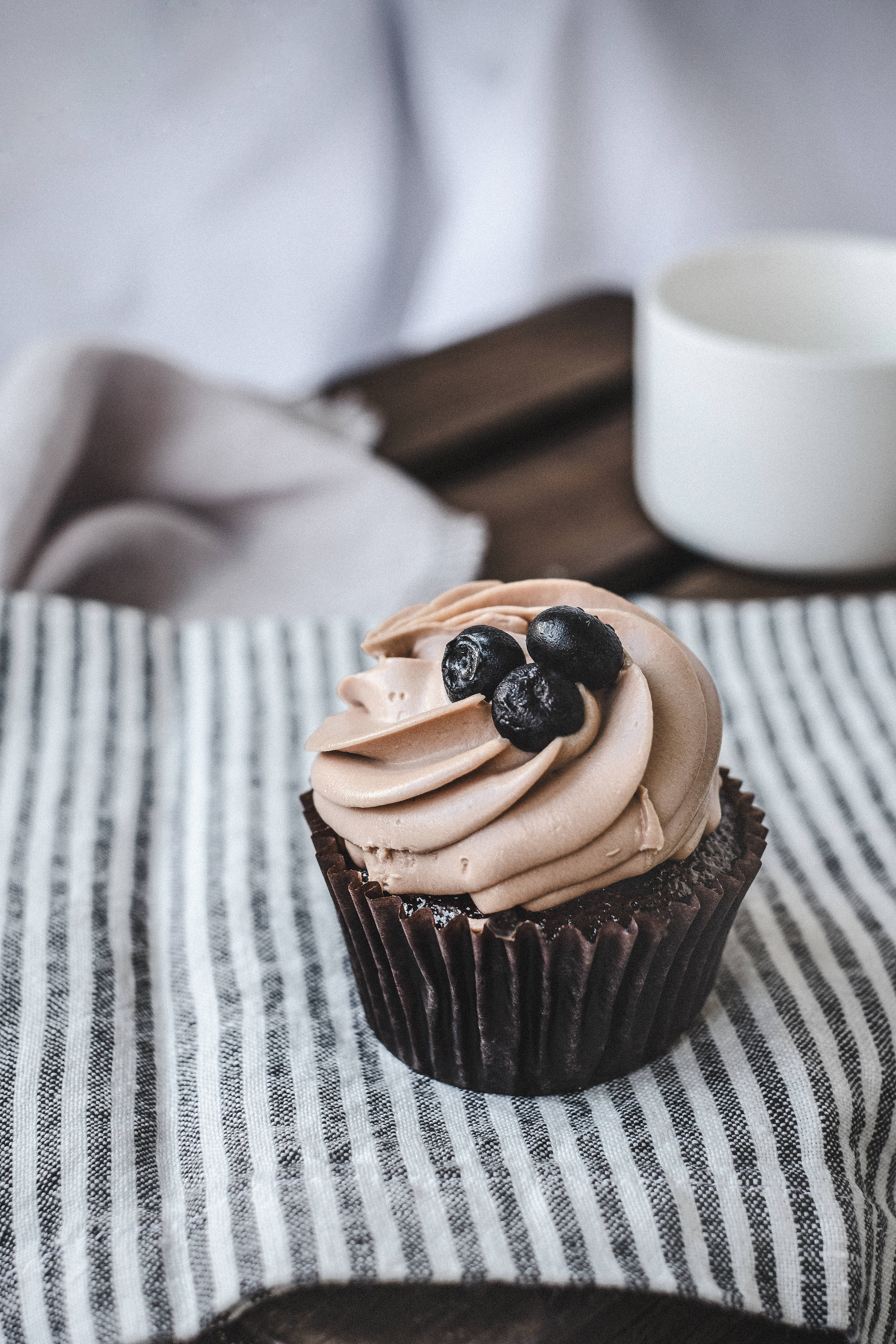 Cupcake 桌布 壁紙 — 一個巧克力紙杯蛋糕，上面有巧克力糖霜漩渦和新鮮藍莓，放在黑白條紋布上。
