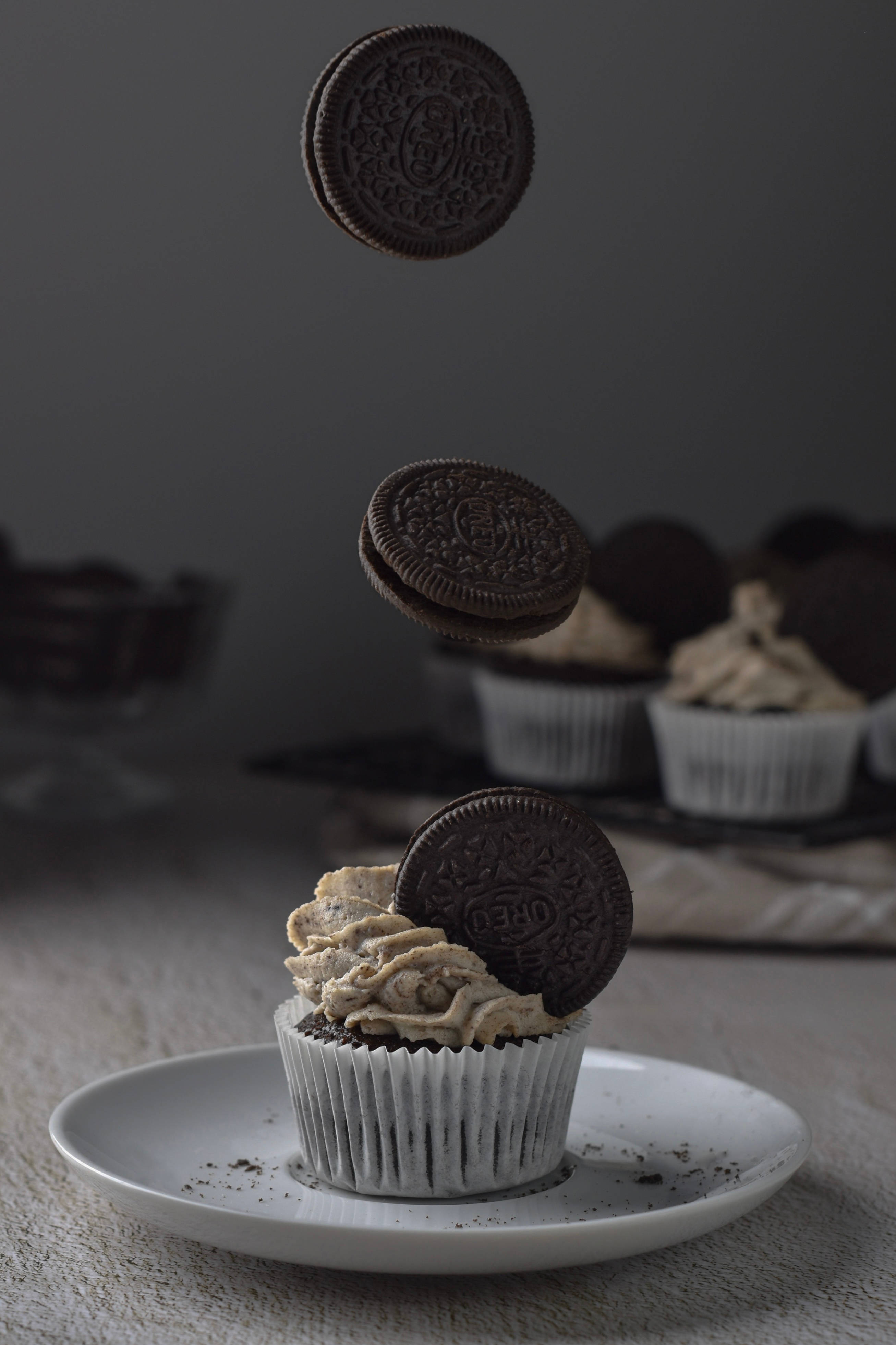 Cupcake 桌布 壁紙 — 一個巧克力紙杯蛋糕配上奶油糖霜，Oreo 餅乾懸浮在蛋糕上方，背景為深灰色。