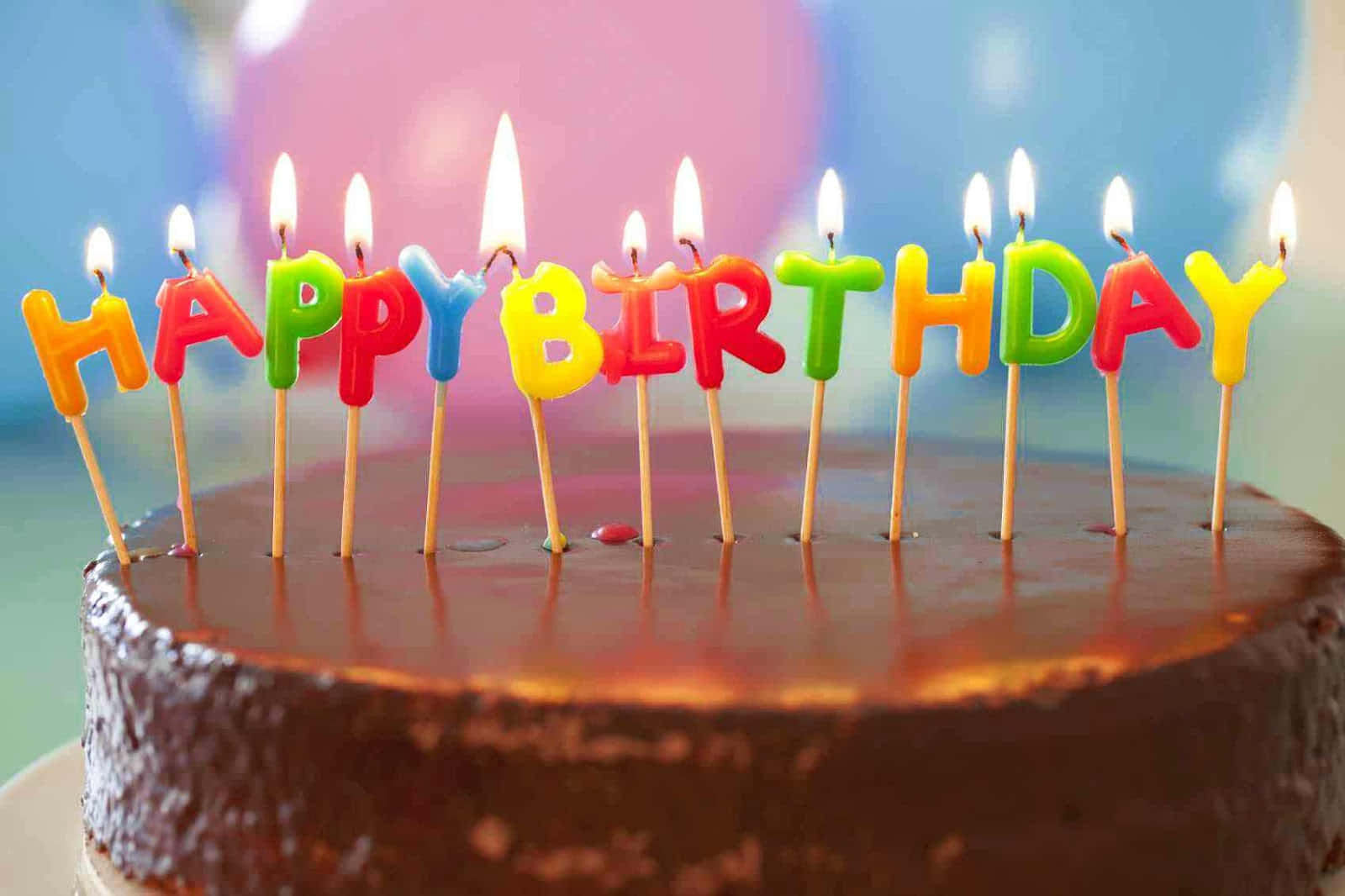 Happy Birthday Cake 桌布 壁紙 — 一個巧克力蛋糕，上面有色彩繽紛的點燃蠟燭拼出 happy birthday，背景柔和模糊。