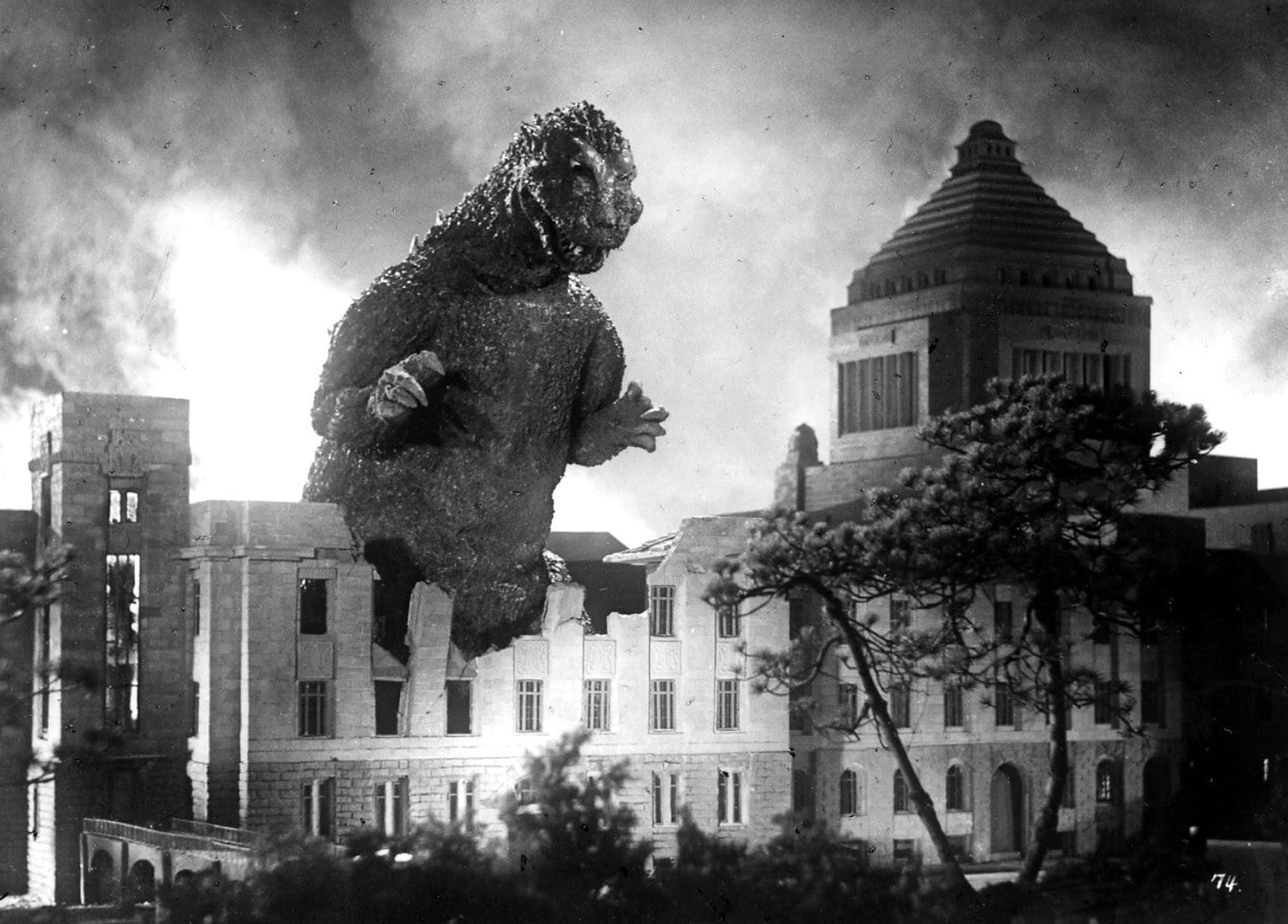 Godzilla 1954 桌布 壁紙 — 一個巨型怪物踩過城市景觀，壓碎建築物，形成戲劇性的黑白場景。