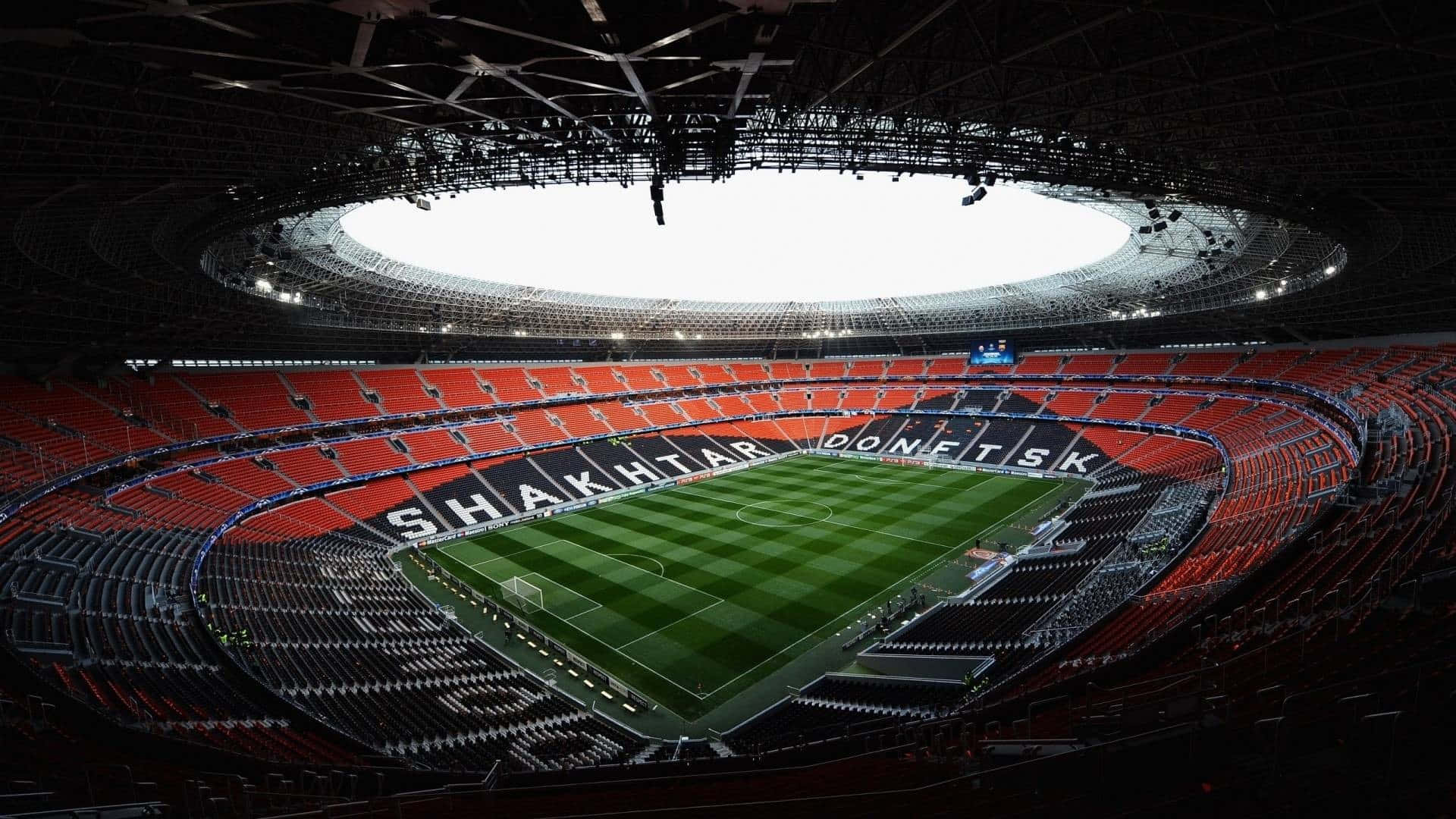 Soccer Stadium 桌布 壁紙 — 一個巨大現代足球場的鳥瞰圖，擁有鮮豔的紅色座椅和一個在明亮圓形天窗下的純淨綠色球場。