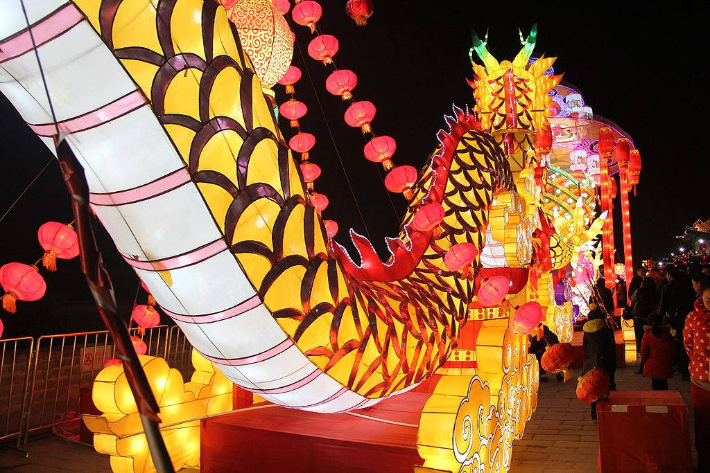 Xian 桌布 壁紙 — 一個巨大發光的黃色龍燈籠，帶有紅色點綴和懸掛的粉紅色燈籠，照亮了夜間節日的街道。