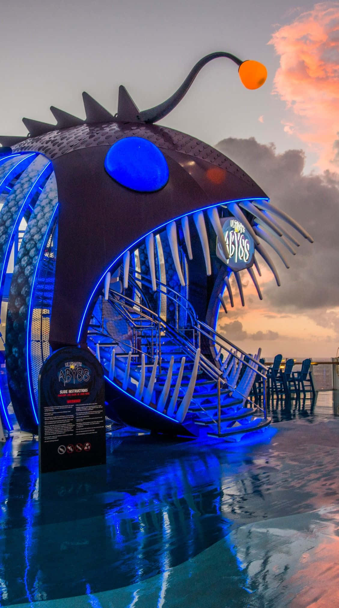 Carnival Vista 桌布 壁紙 — 一個巨大發光藍色琵琶魚雕塑，擁有鋒利牙齒和橙色誘餌，在日落時聳立於泳池之上。