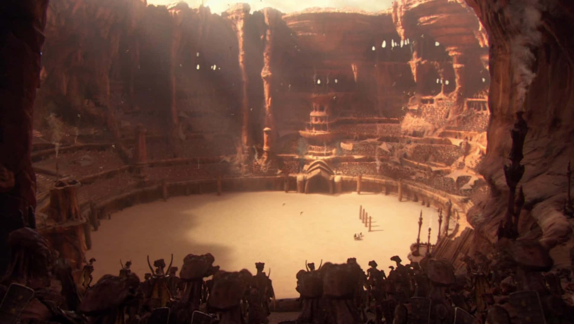 The Geonosian Arena 桌布 壁紙 — 一個巨大的古老競技場雕刻在洞穴般的岩壁上，戰士們站在競技場中，沐浴在溫暖的金色光芒下。