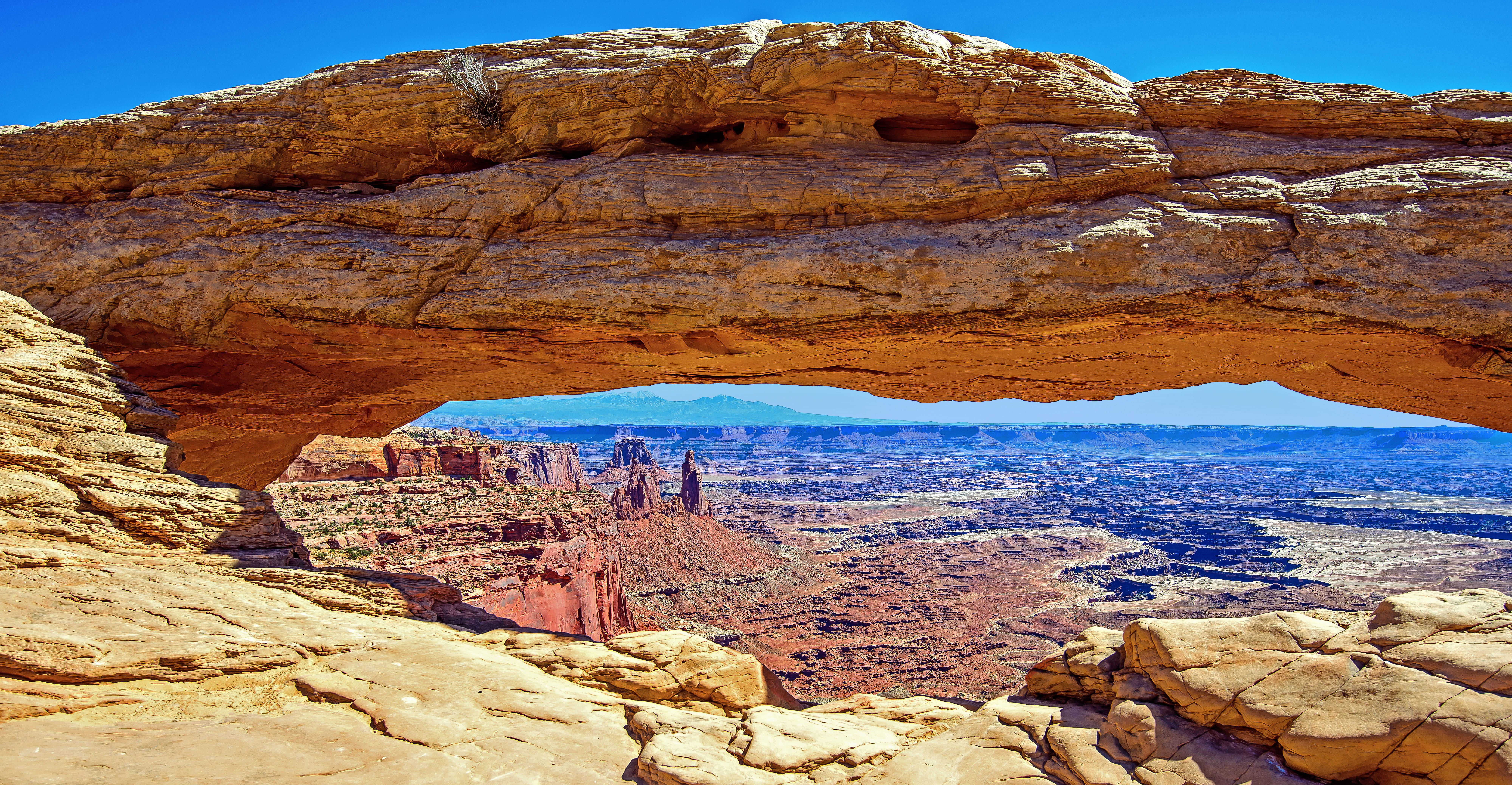 Canyonlands National Park 桌布 壁紙 — 一個巨大的天然砂岩拱門框住了廣闊的沙漠峽谷，上方是清澈的藍天。