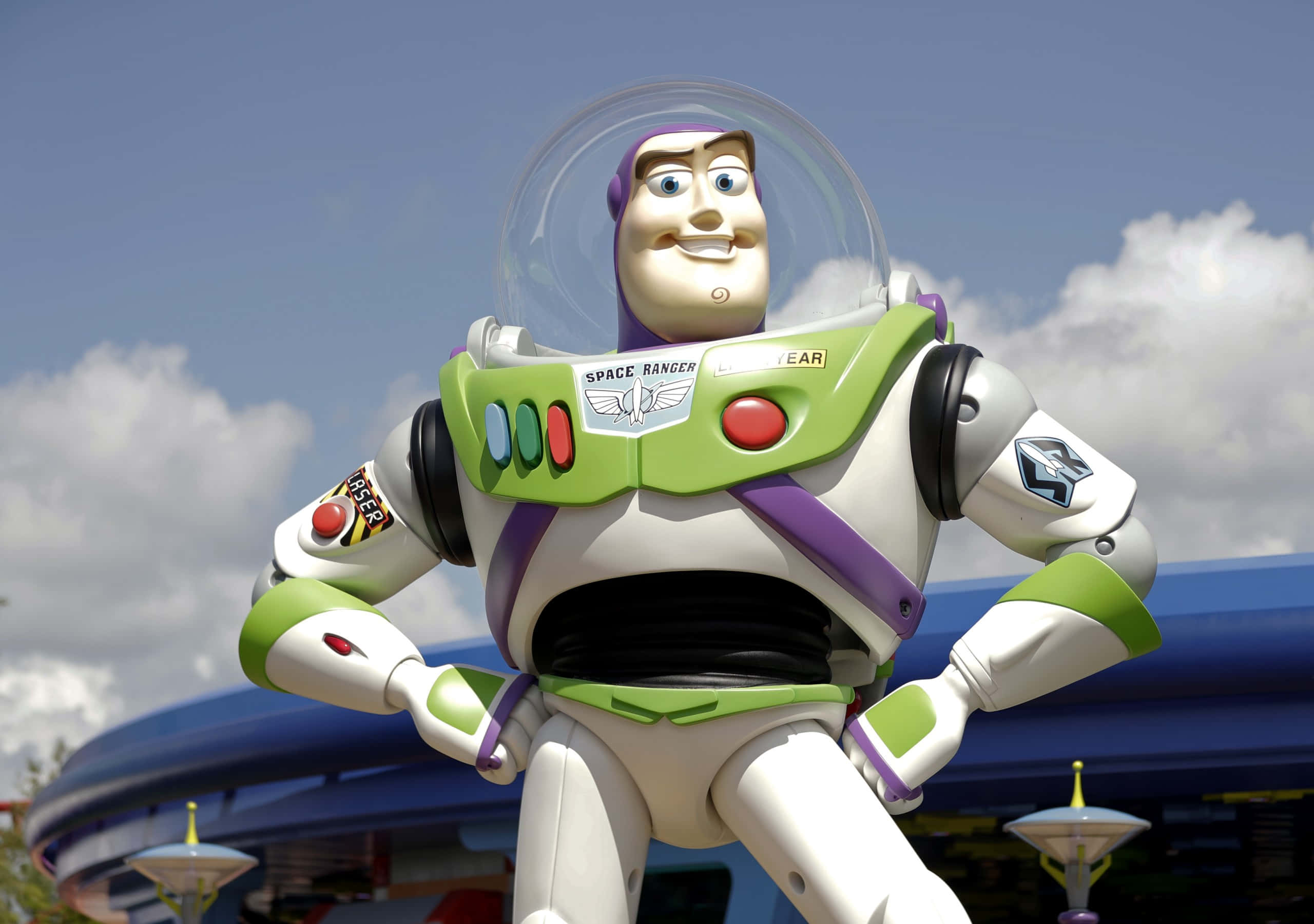 Buzz Lightyear 桌布 壁紙 — 一個巨大的巴斯光年雕像自信地站在明亮的藍天和蓬鬆的白雲前。