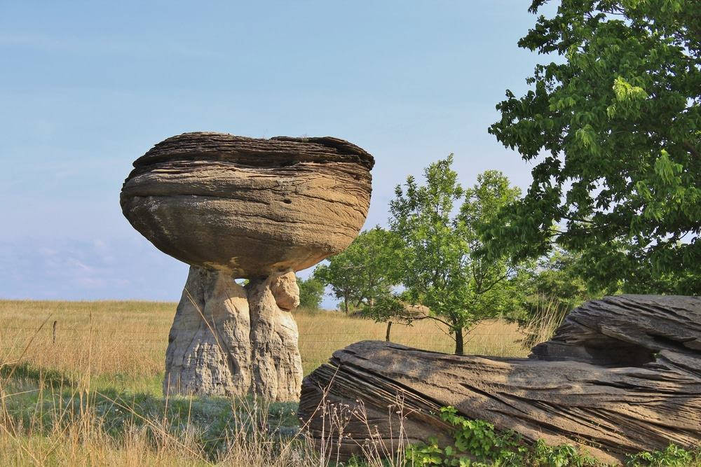 Rocks 桌布 壁紙 — 一個巨大的平衡岩石聳立在陽光明媚的草地上，周圍有綠樹和清澈的藍天。