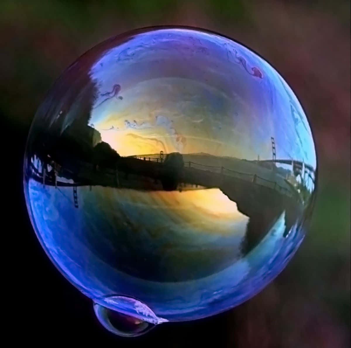Bubble 桌布 壁紙 — 一個巨大的彩虹色泡泡，以夢幻般的魚眼視角反射出橋樑和山丘上的金色日落。