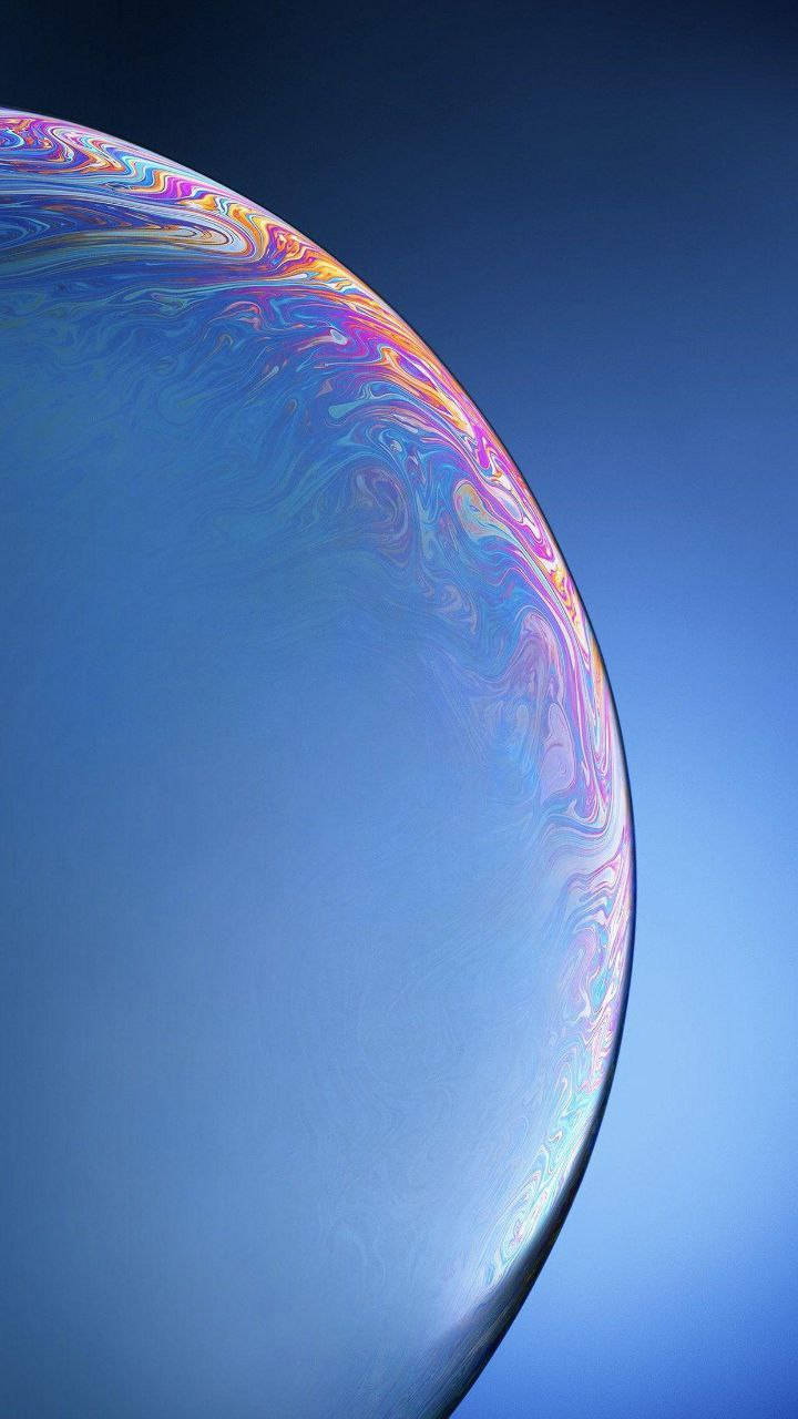 iPhone 桌布 壁紙 — 一個巨大的彩虹色肥皂泡在晴朗的藍天上漂浮，邊緣呈現旋轉的彩虹色。