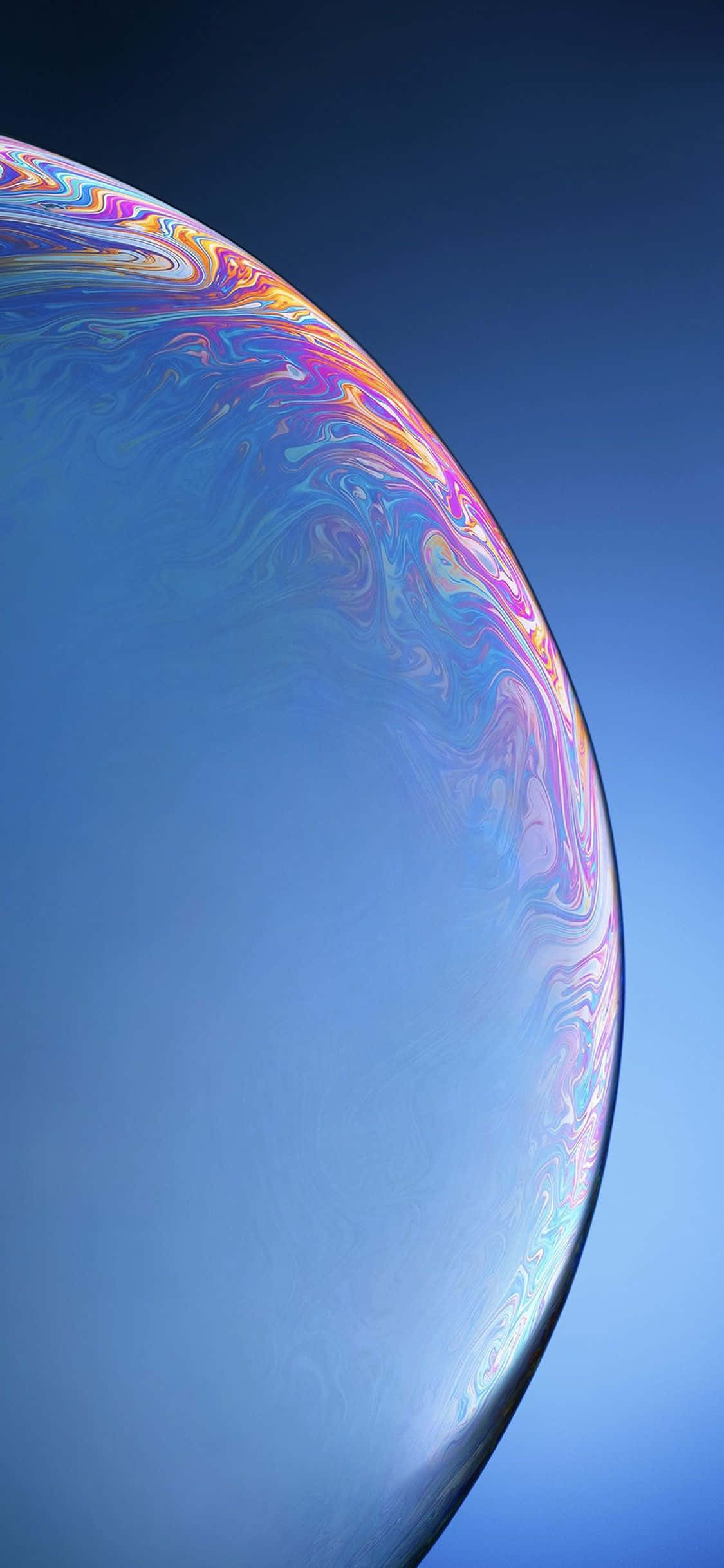 Apple iPhone Xs Max 桌布 壁紙 — 一個巨大的彩虹色肥皂泡在漸變藍色的天空中漂浮，其彎曲表面呈現出旋轉的彩虹色。