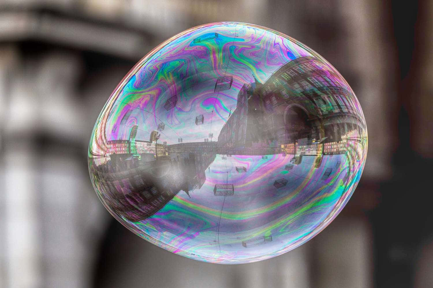 Bubble 桌布 壁紙 — 一個巨大的彩虹色肥皂泡懸浮在半空中，反射出扭曲的城市景觀，帶有鮮豔的彩虹色調。