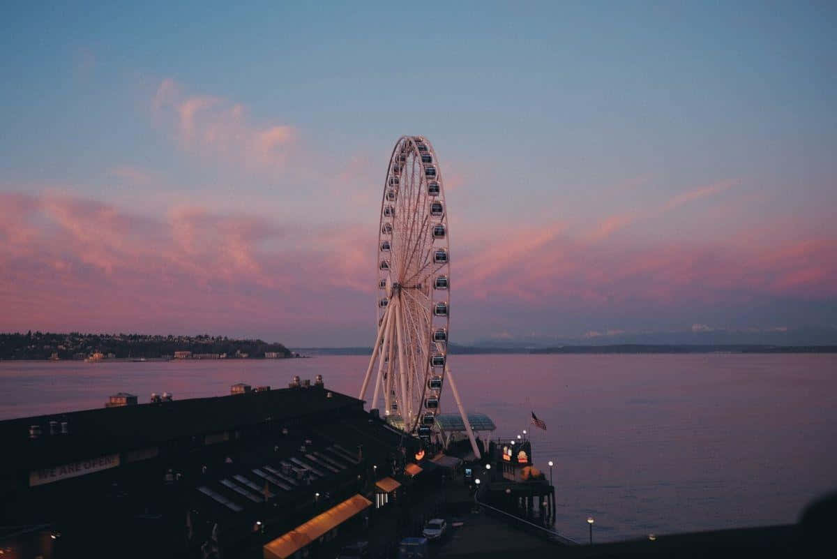 Vsco Laptop 桌布 壁紙 — 一個巨大的摩天輪在暮色天空下呈現剪影，天空被柔和的粉紅色和紫色雲彩點綴，下方是平靜的海濱。