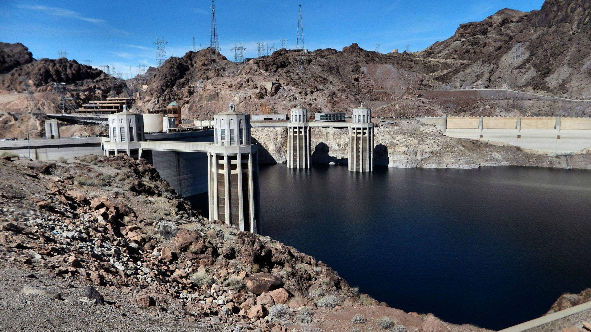 Lake 桌布 壁紙 — 一個巨大的混凝土水壩在晴朗的藍天下，將深藍色的水擋在崎嶇的棕色沙漠懸崖前。