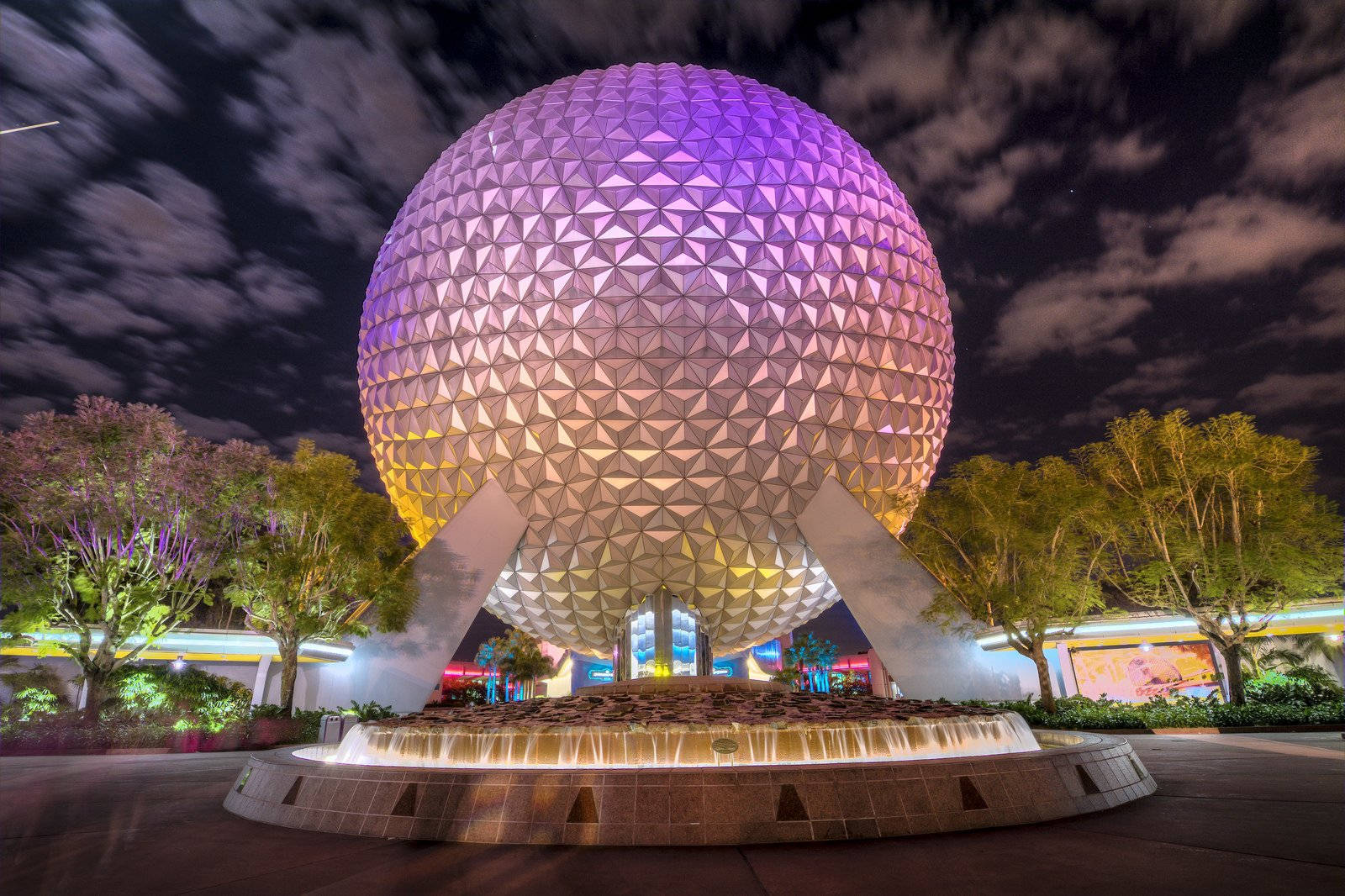 Universal Studios 桌布 壁紙 — 一個巨大的測地線球體在噴泉和樹木上方的星空夜空下發出紫色和金色的光芒。