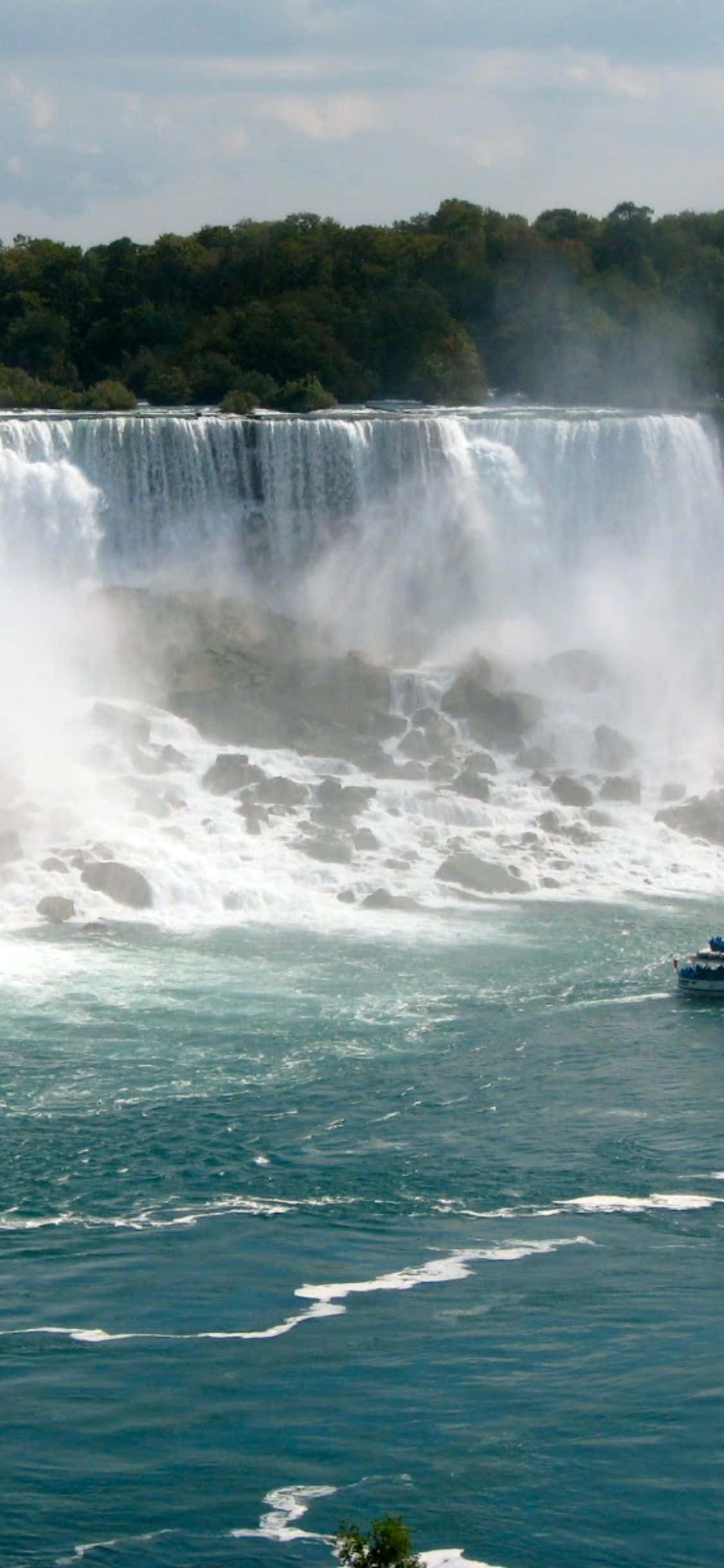 Niagara Falls 桌布 壁紙 — 一個巨大的瀑布從岩石懸崖上傾瀉而下，流入下方湍急的碧綠河流，天空部分多雲。