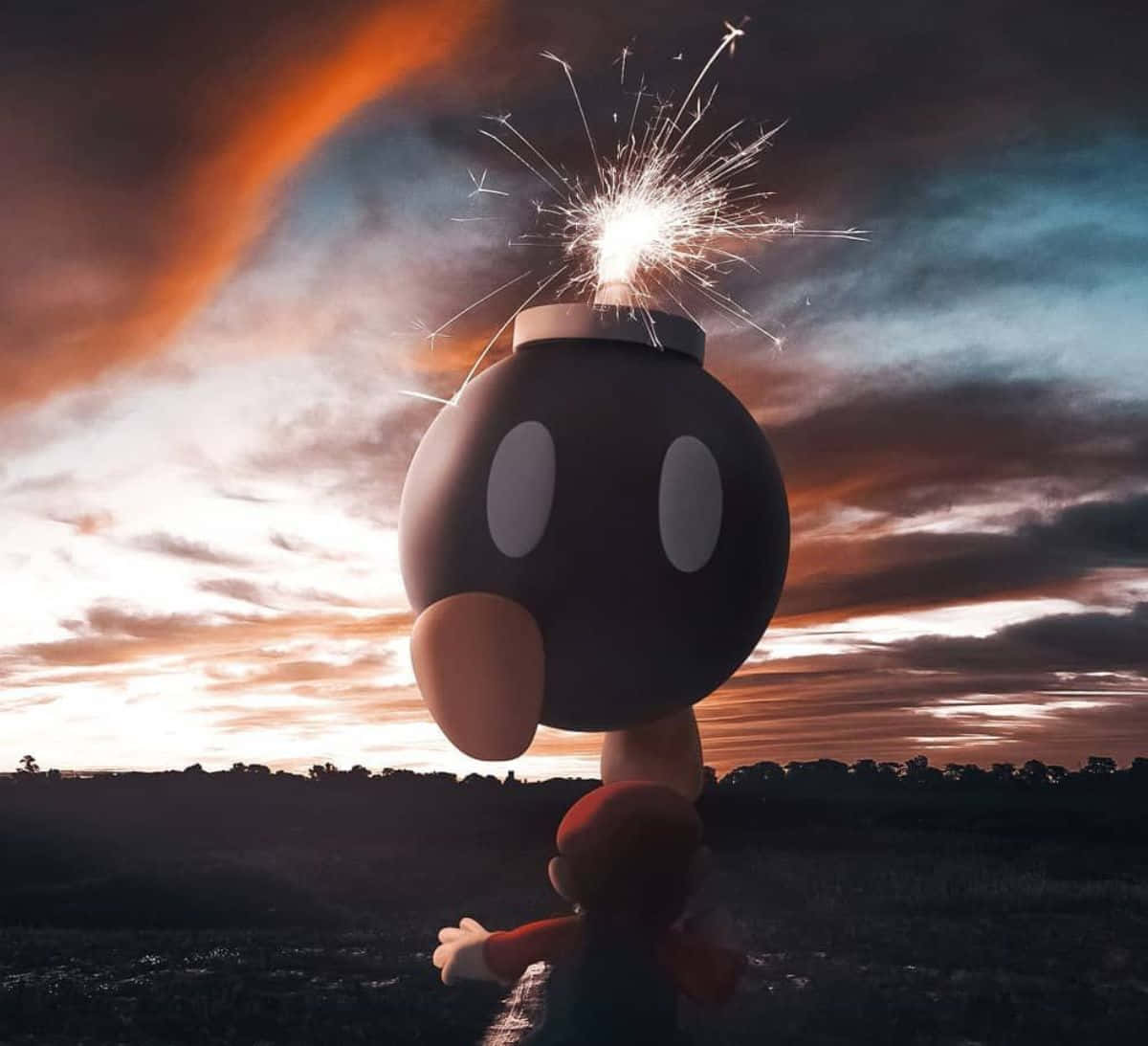 Bob-omb 桌布 壁紙 — 一個巨大的炸彈兵頭頂點燃的煙火棒，站在小馬力歐上方，背景是熾熱的夕陽天空。