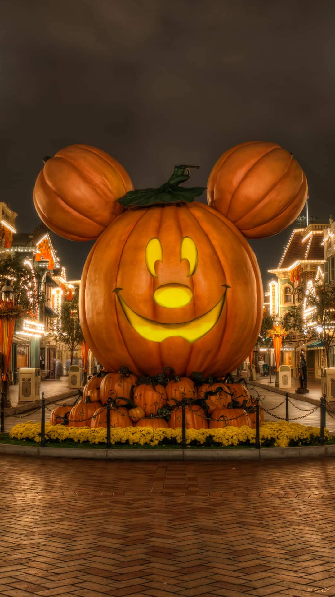 Halloween Pumpkin 桌布 壁紙 — 一個巨大的發光傑克南瓜燈，形狀像米奇老鼠，在夜晚的萬聖節主題街道上明亮地微笑。