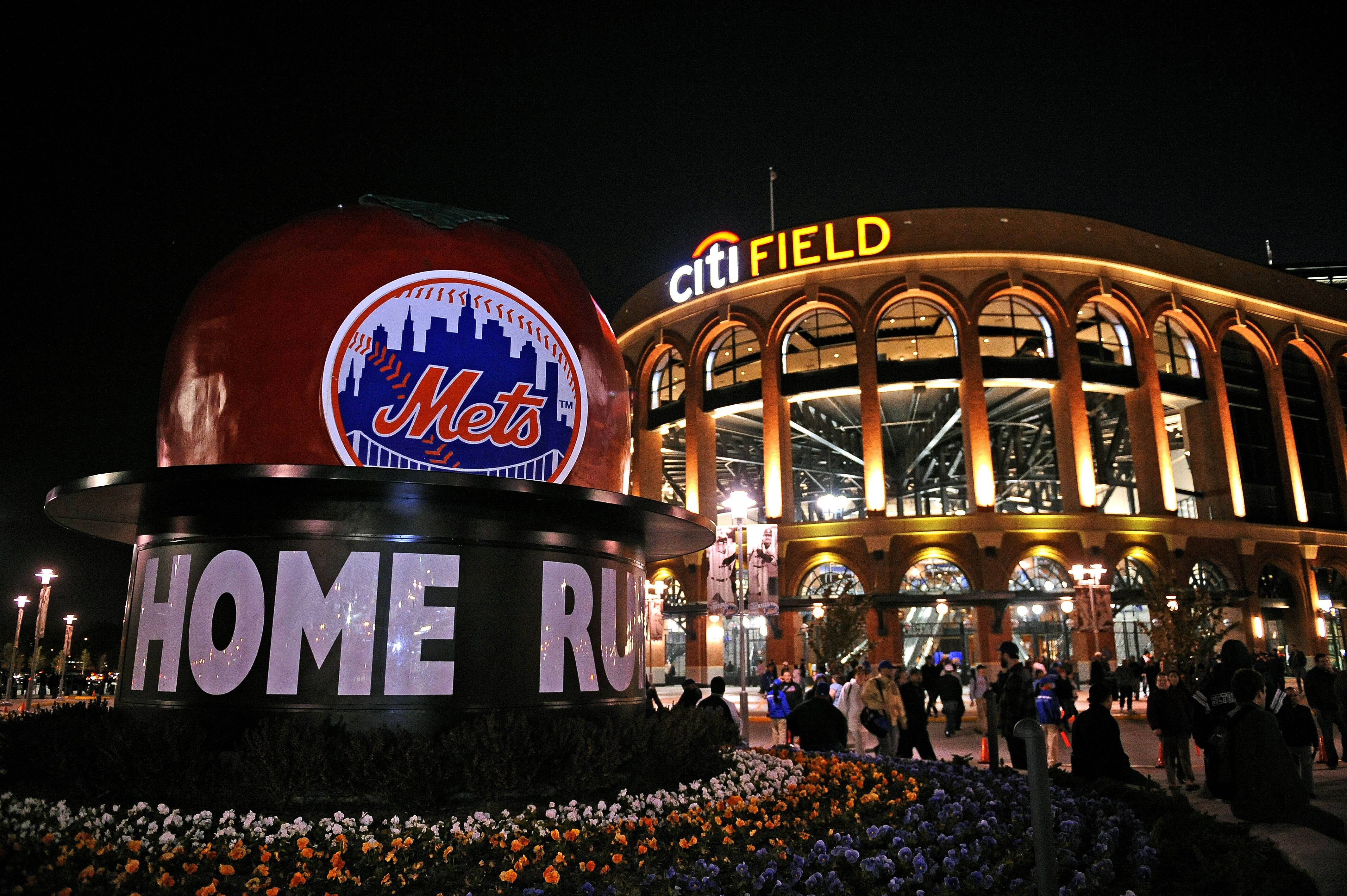 New 桌布 壁紙 — 一個巨大的發光蘋果，帶有Mets標誌和「HOME RUN」文字，夜晚矗立在Citi Field前，周圍環繞著色彩繽紛的花朵和球迷。