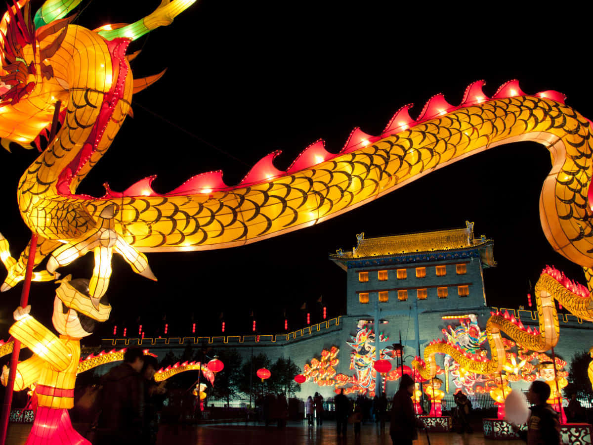 Chinese New Year 2022 桌布 壁紙 — 一個巨大的發光金色龍燈籠在夜間拱起於歷史悠久的中國門樓之上，由溫暖的燈光照亮，下方有人群。