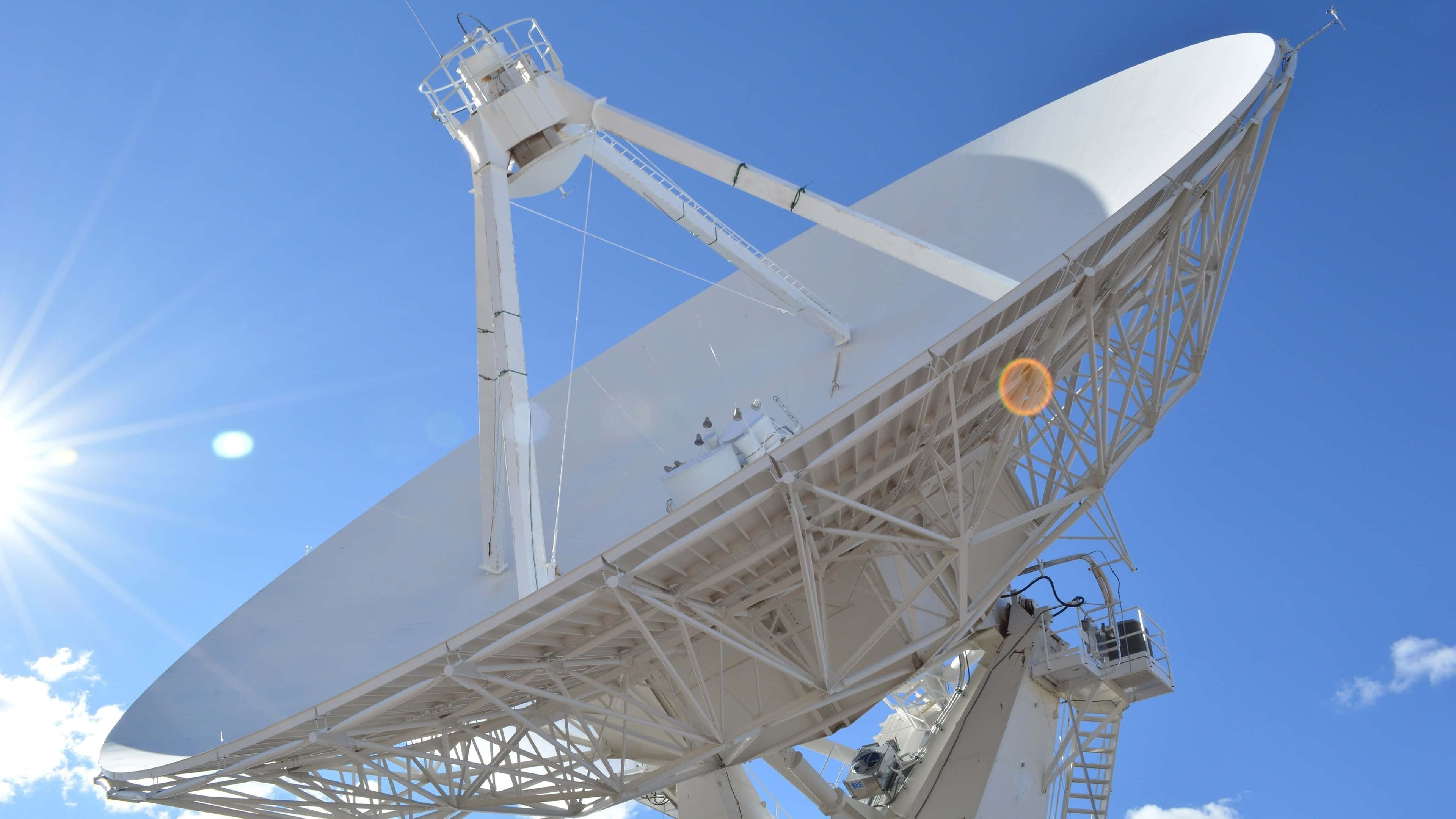 Satellite 桌布 壁紙 — 一個巨大的白色衛星天線主宰著晴朗的藍天，太陽在其後方明亮地照耀。