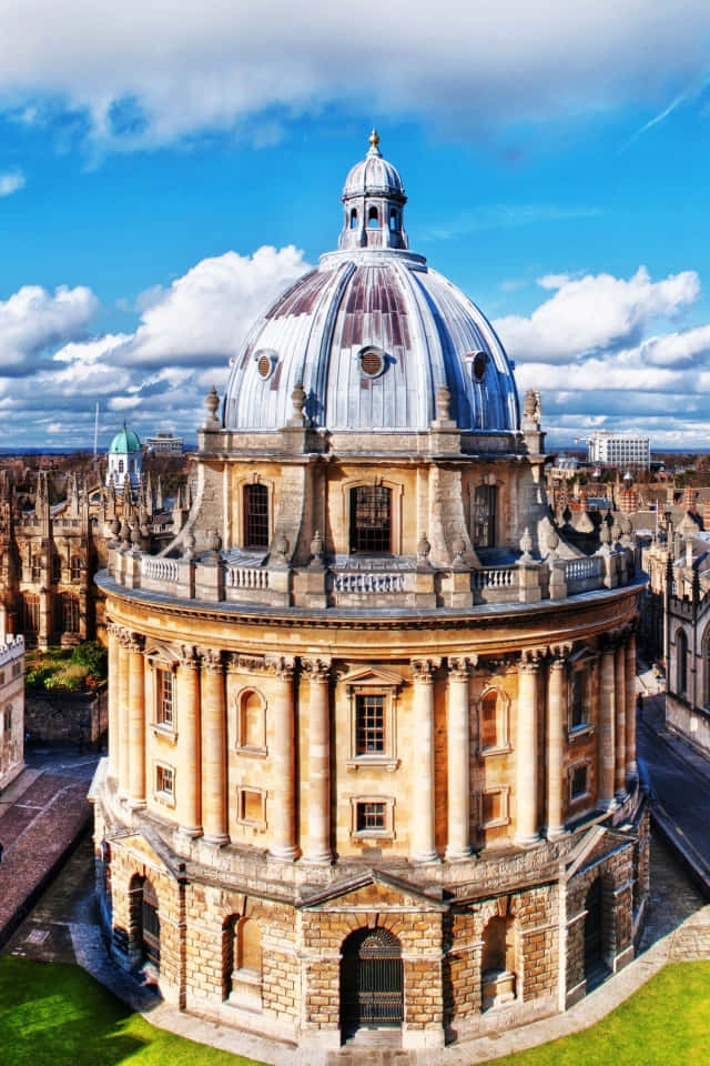 England 桌布 壁紙 — 一個巨大的石穹頂，藍天白雲，聳立在歷史悠久的牛津大學建築之上。