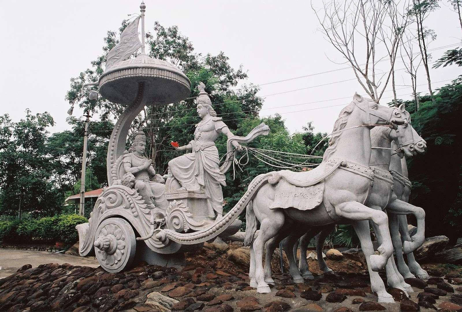 Indian 桌布 壁紙 — 一個巨大的石雕描繪了一個神話人物駕駛著由兩匹馬拉著的戰車穿過鬱鬱蔥蔥的綠色公園。