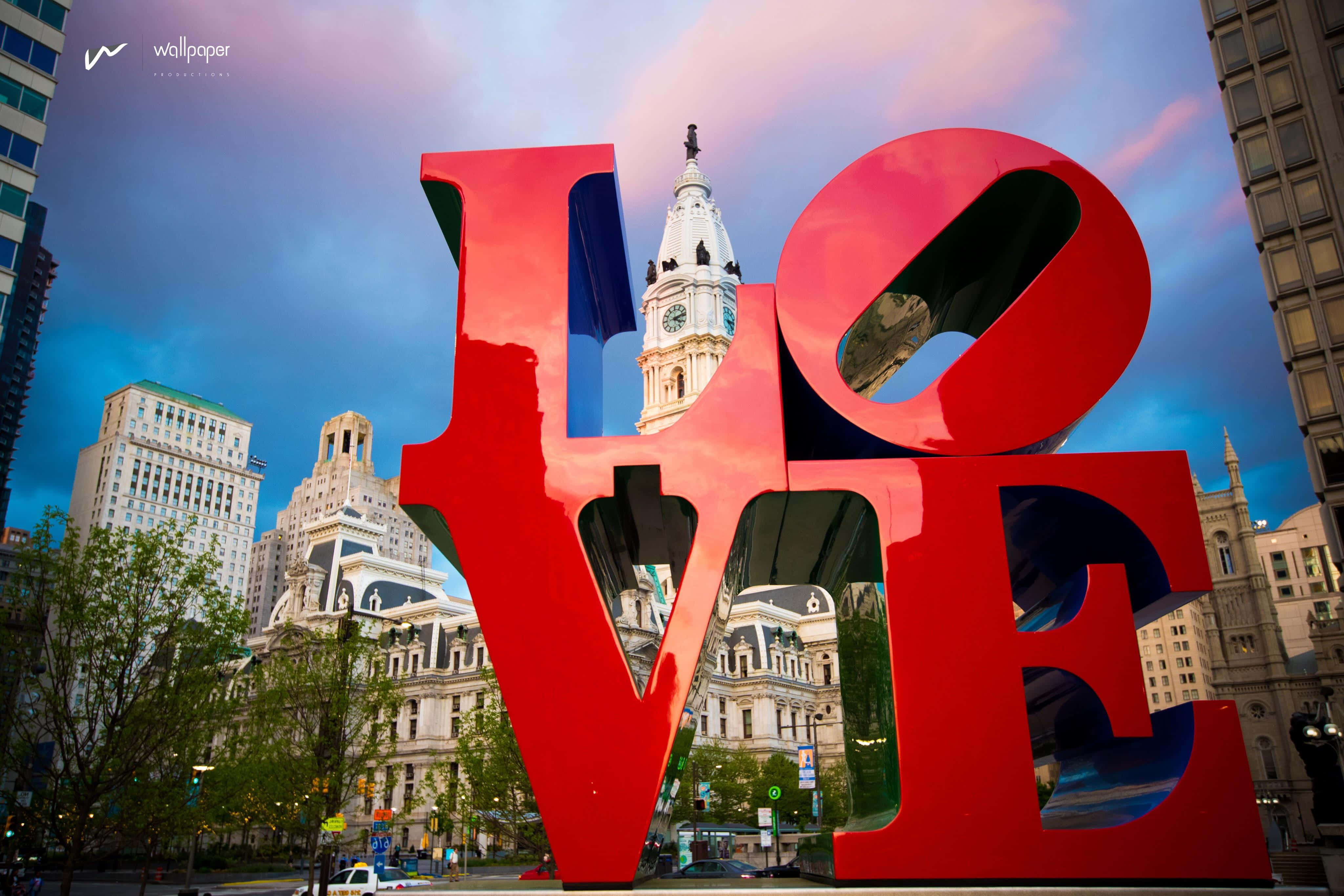 Philly 桌布 壁紙 — 一個巨大的紅色LOVE雕塑矗立在城市廣場上，背後可見歷史建築和鐘樓，在暮色天空下。