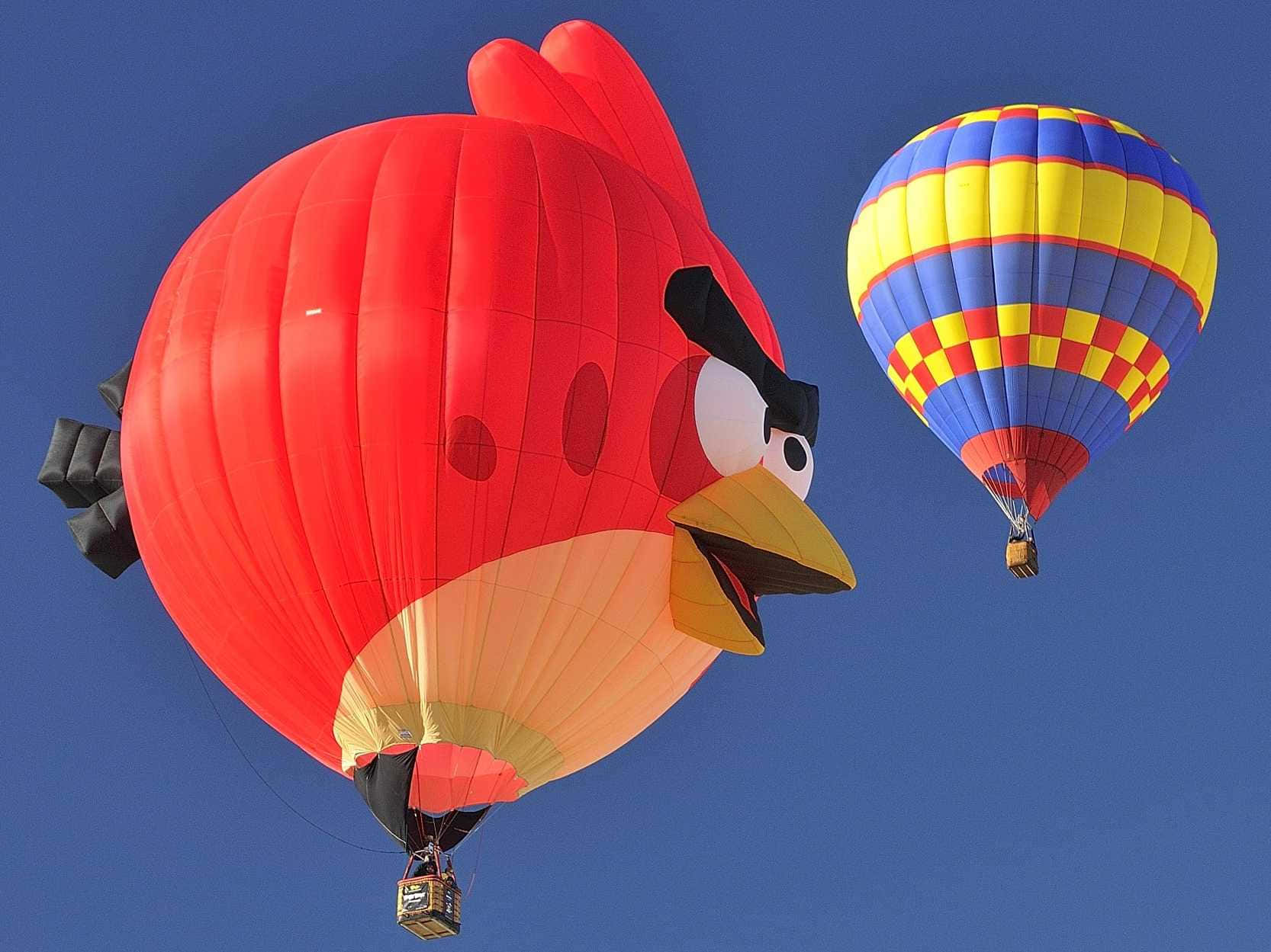 Hot Air Balloon 桌布 壁紙 — 一個巨大的紅色憤怒鳥熱氣球在晴朗的藍天中，旁邊漂浮著一個色彩繽紛的格子氣球。