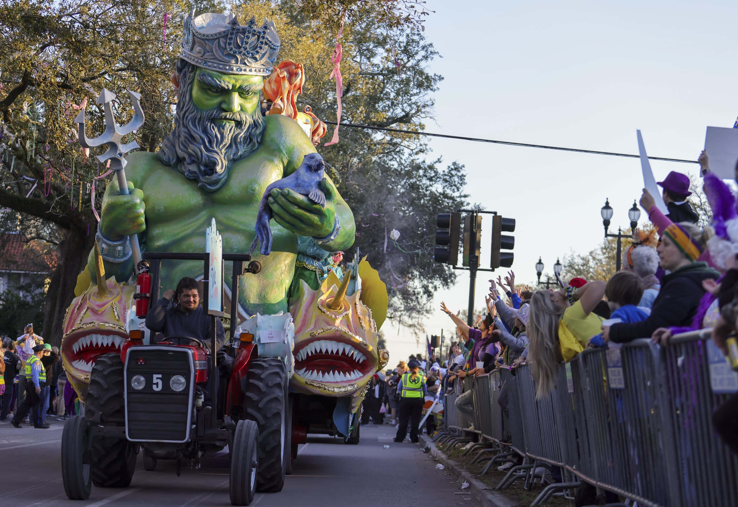 Mardi Gras 桌布 壁紙 — 一個巨大的綠色海神花車，帶有鯊魚頭和三叉戟，在街上遊行，人群在路障後面歡呼。