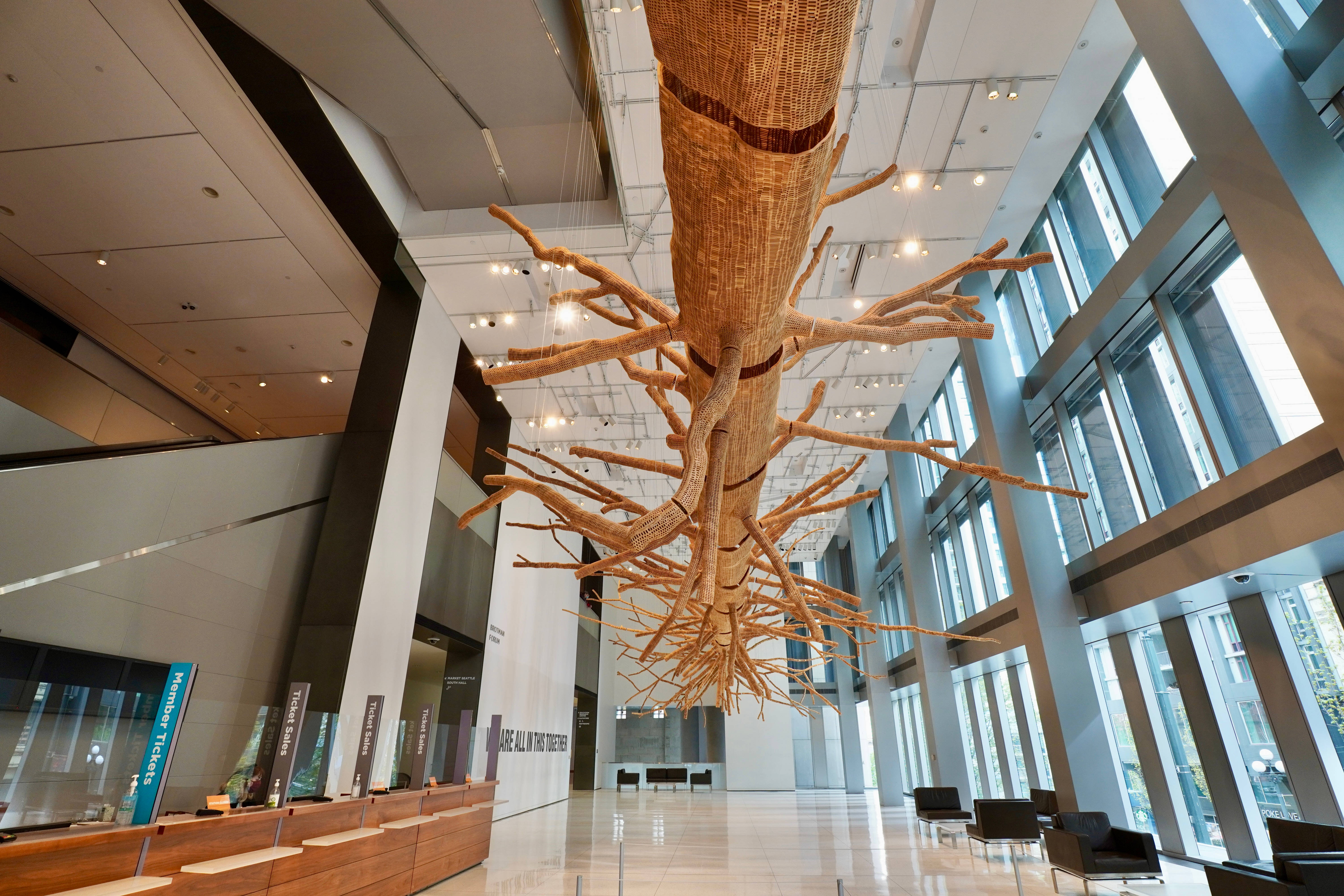Museum 桌布 壁紙 — 一個巨大的編織樹雕塑懸掛在現代玻璃牆大廳的天花板上，搭配時尚家具和自然光。
