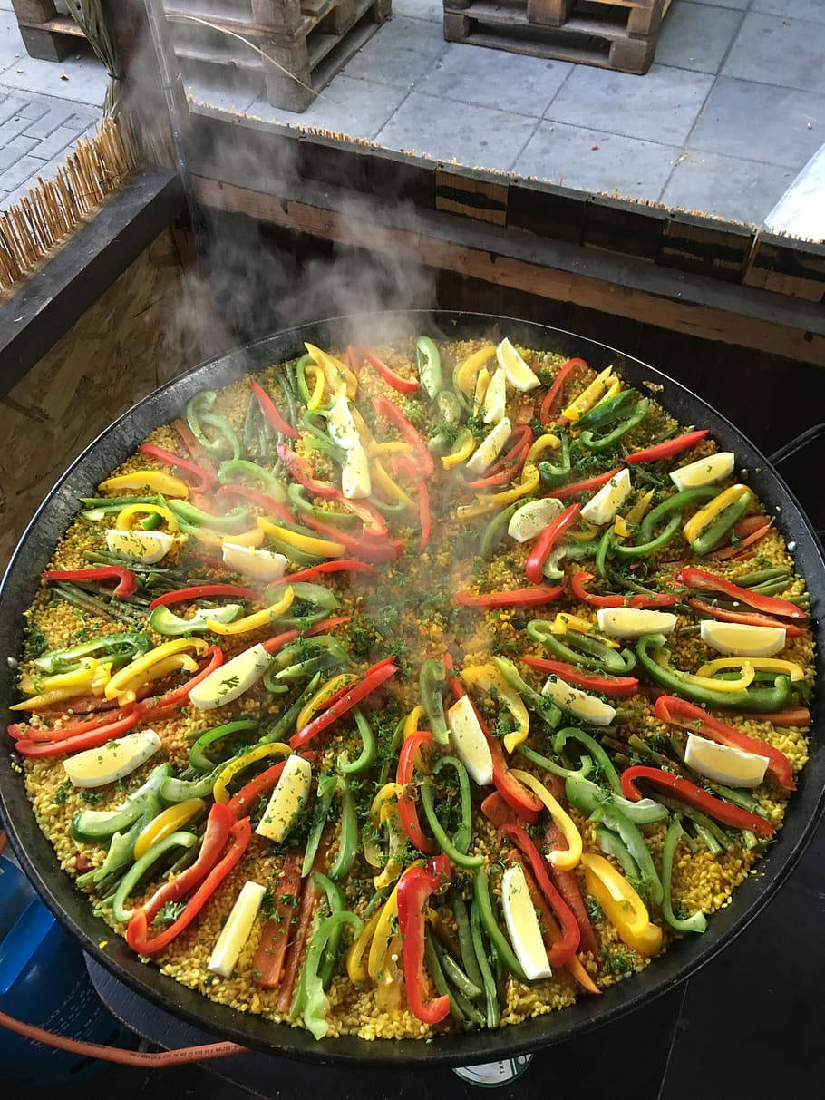 Rice 桌布 壁紙 — 一個巨大的蒸氣騰騰的西班牙大鍋飯鍋，裝滿了色彩繽紛的燈籠椒和檸檬片，在瓷磚露台上滋滋作響。