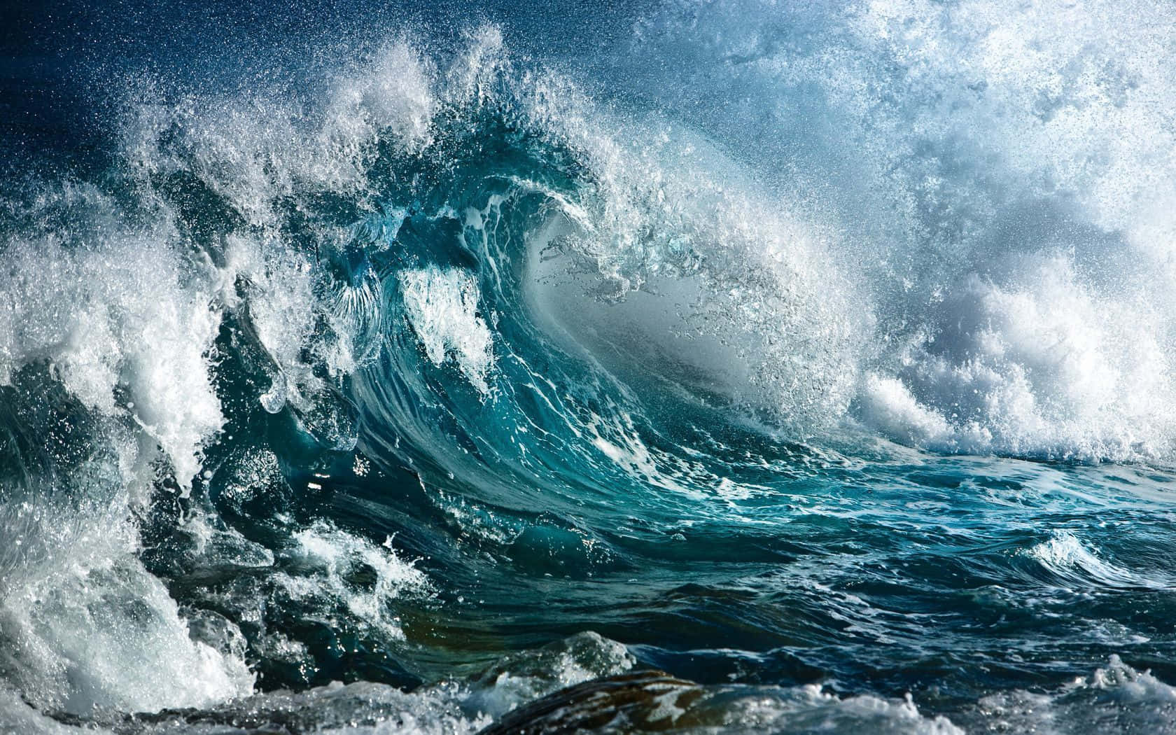 Ocean Waves 桌布 壁紙 — 一個巨大的藍綠色海浪強力地捲曲在頭頂，帶著泡沫般的白色浪花，映襯著深藍色的海洋。