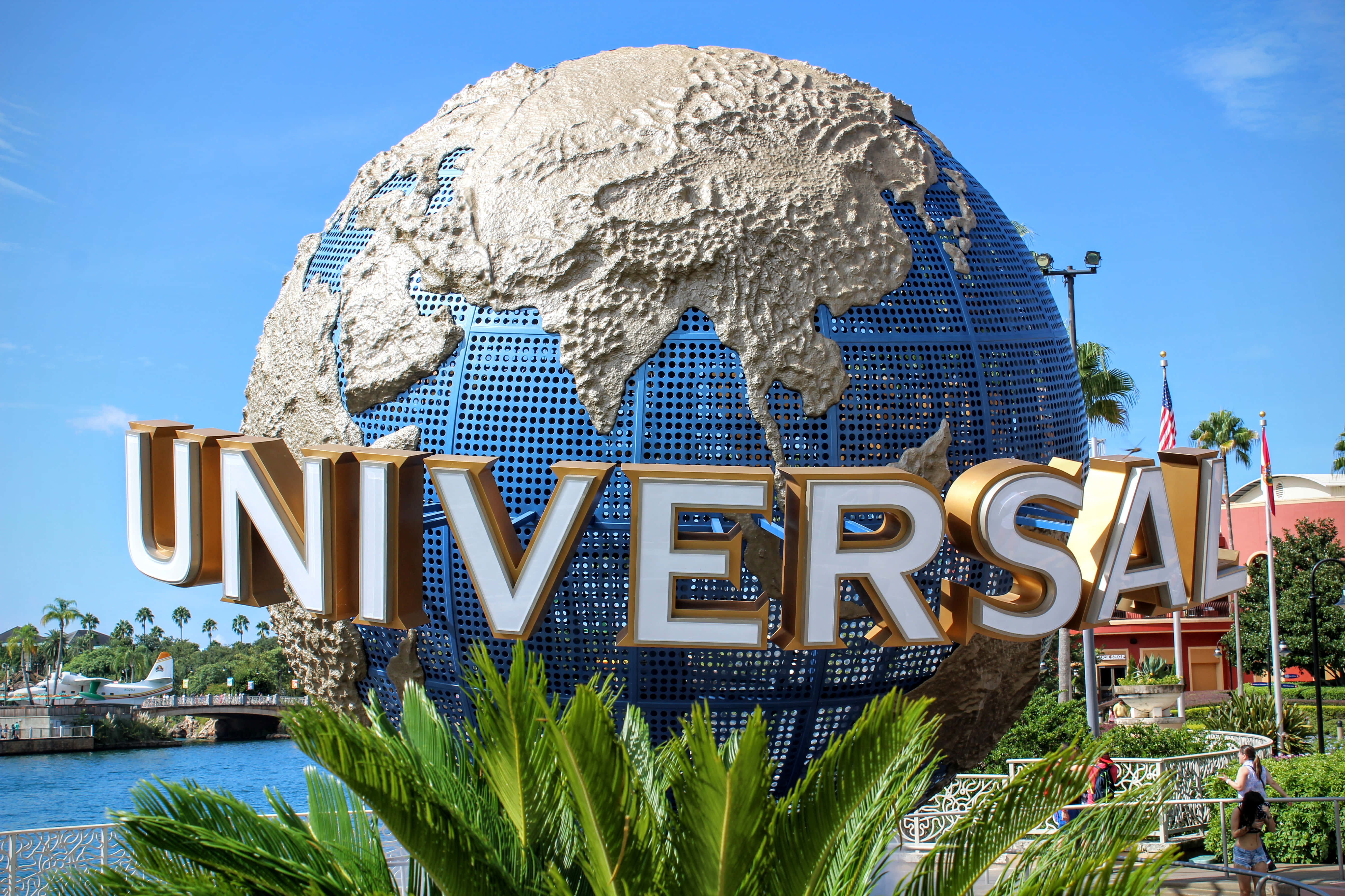 Universal 桌布 壁紙 — 一個巨大的藍色地球儀，帶有紋理米色的大陸，矗立在醒目的金色字母後面，在晴朗的藍天下拼寫出UNIVERSAL。