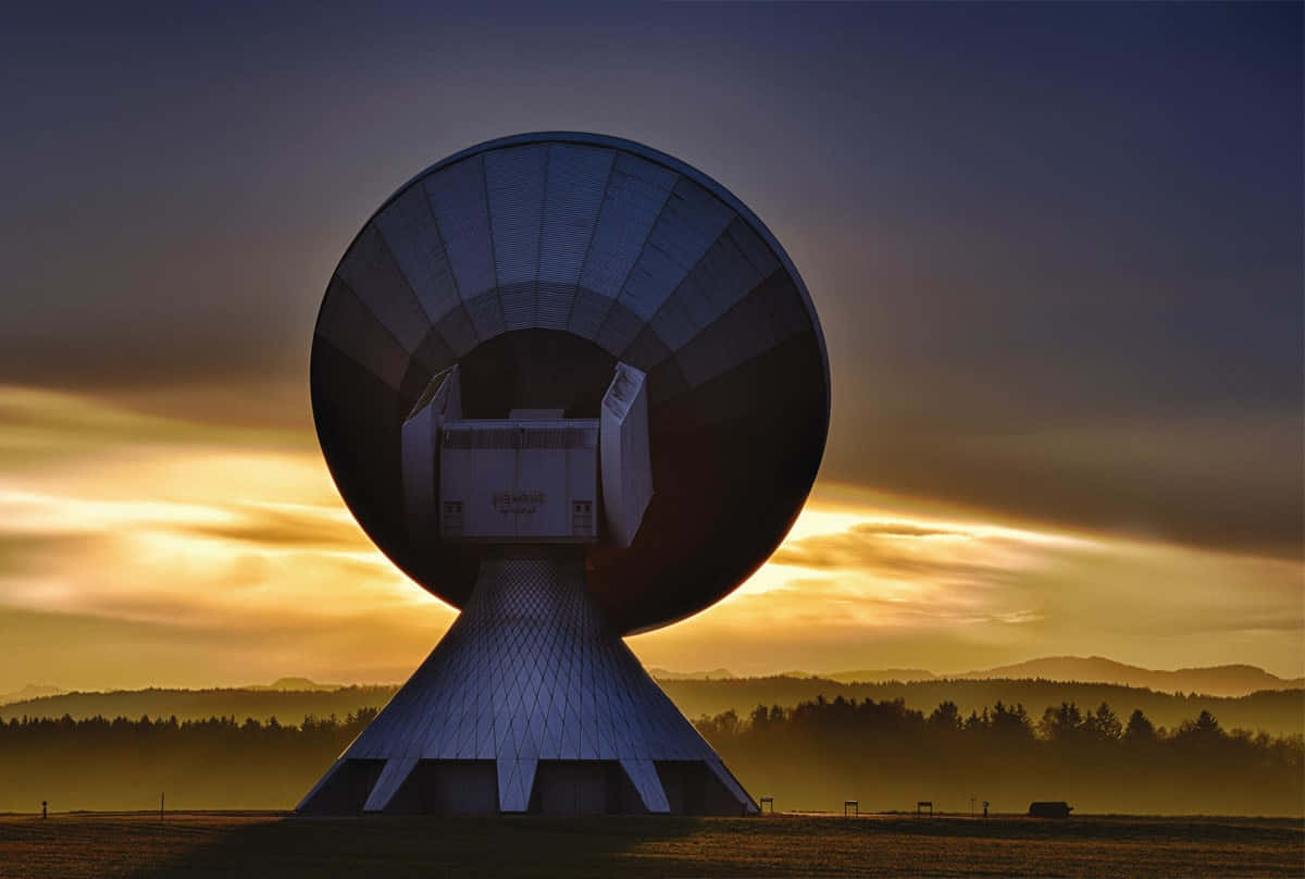 Satellite Technology 桌布 壁紙 — 一個巨大的衛星天線在戲劇性的日落天空下呈現剪影，天空中有金色的雲彩和遠山。