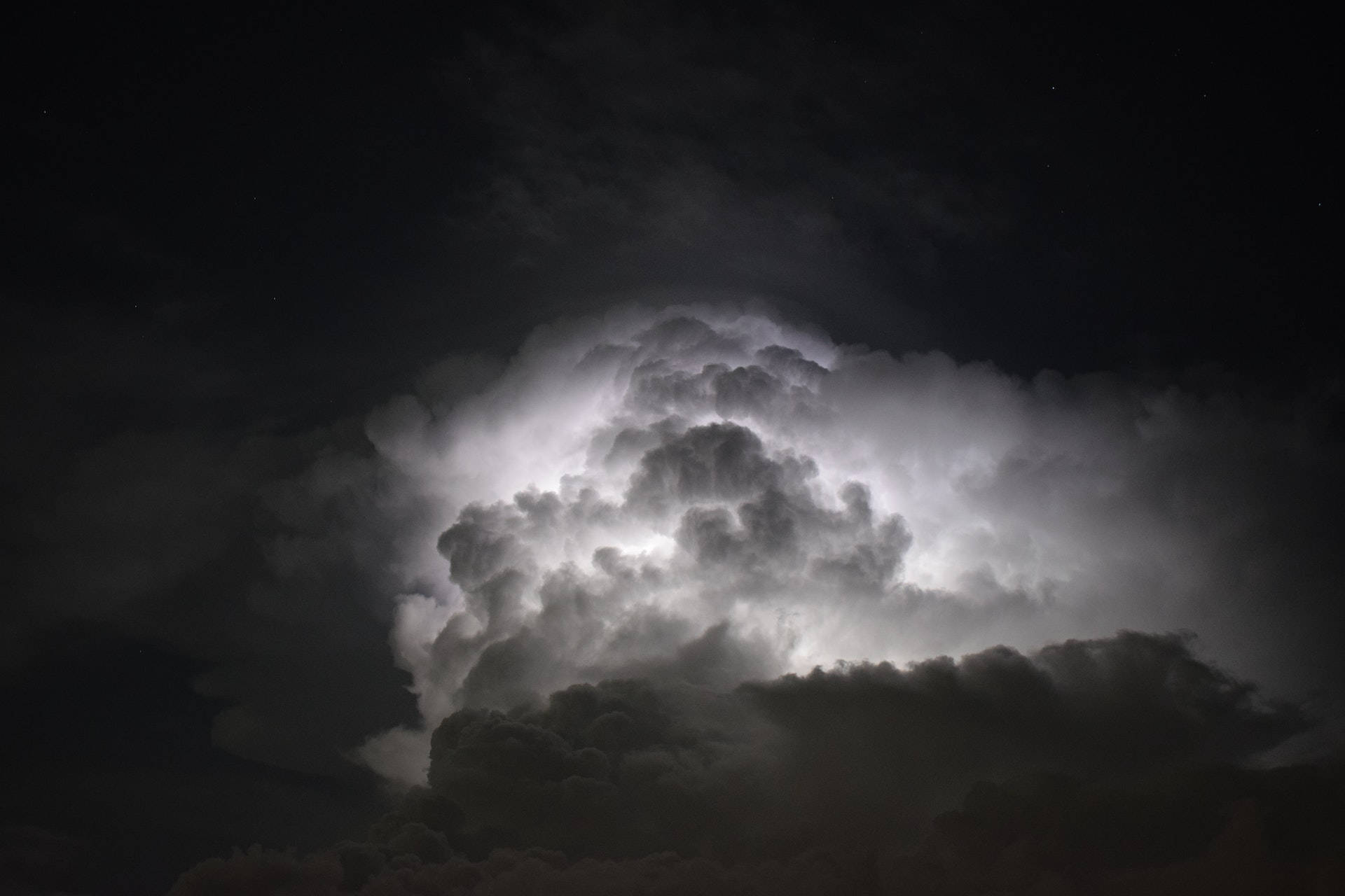 高清 桌布 壁紙 — 一個巨大的雷暴雲，被閃電照亮，映襯著繁星點點的夜空。