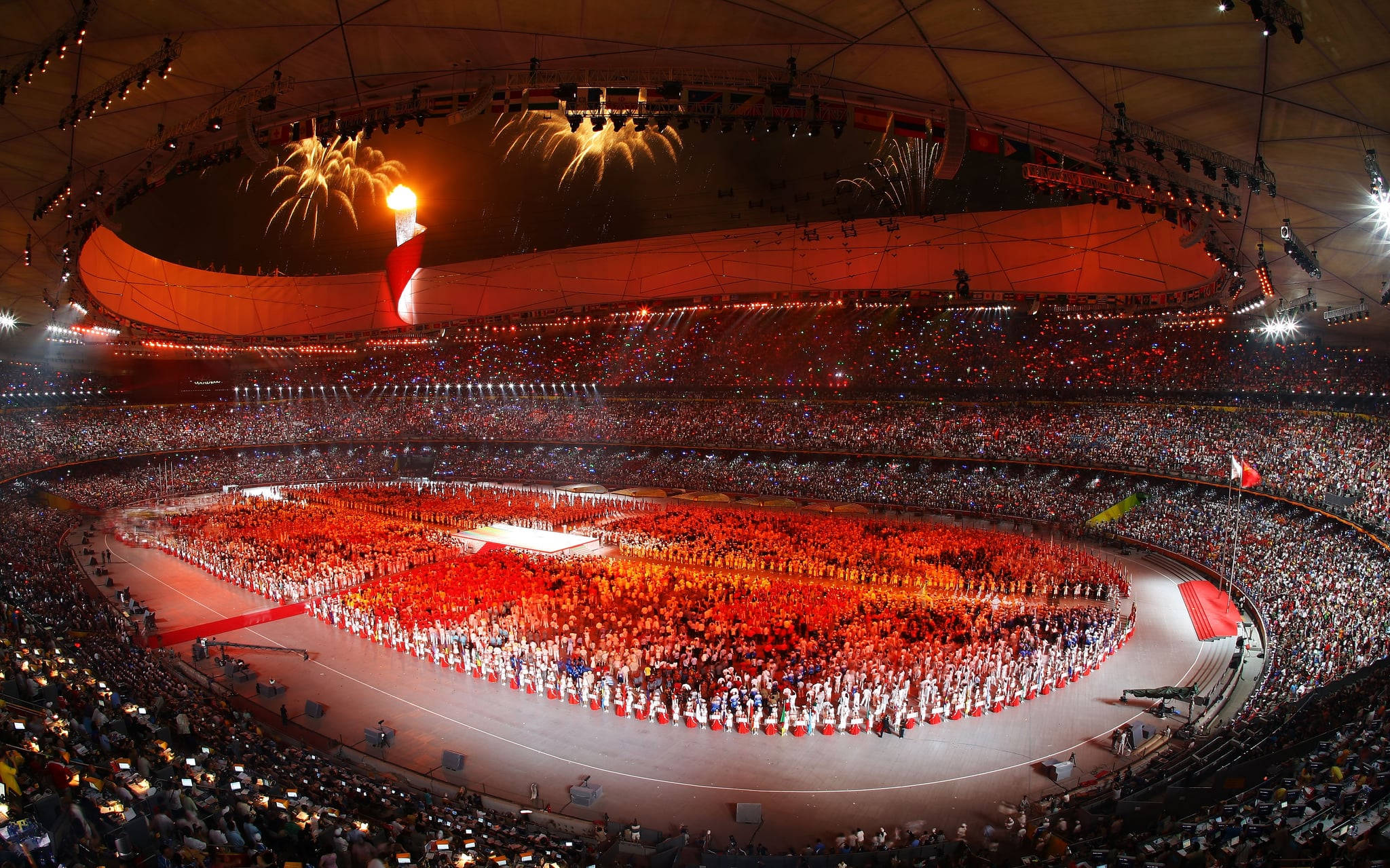 Winter Olympics 桌布 壁紙 — 一個巨大的體育場擠滿了觀眾，煙火在奧運聖火上方爆炸，場面壯觀的開幕典禮。