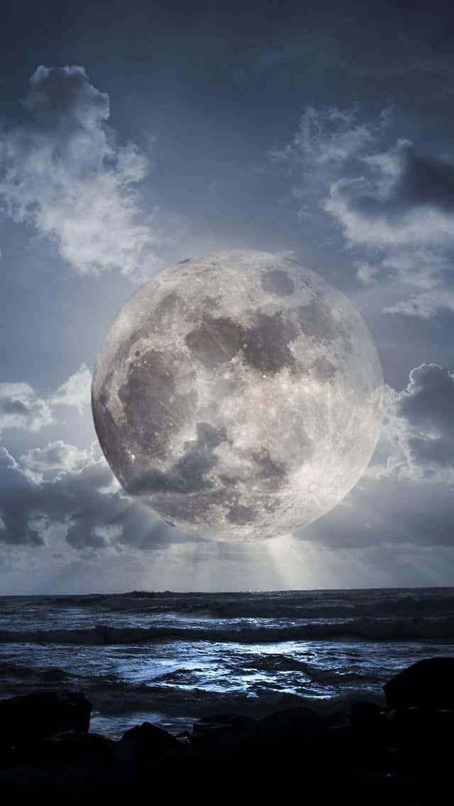 640x1136 桌布 壁紙 — 一個巨大而細節豐富的滿月從暴風雨的海面上升起，透過烏雲散發出空靈的光芒。