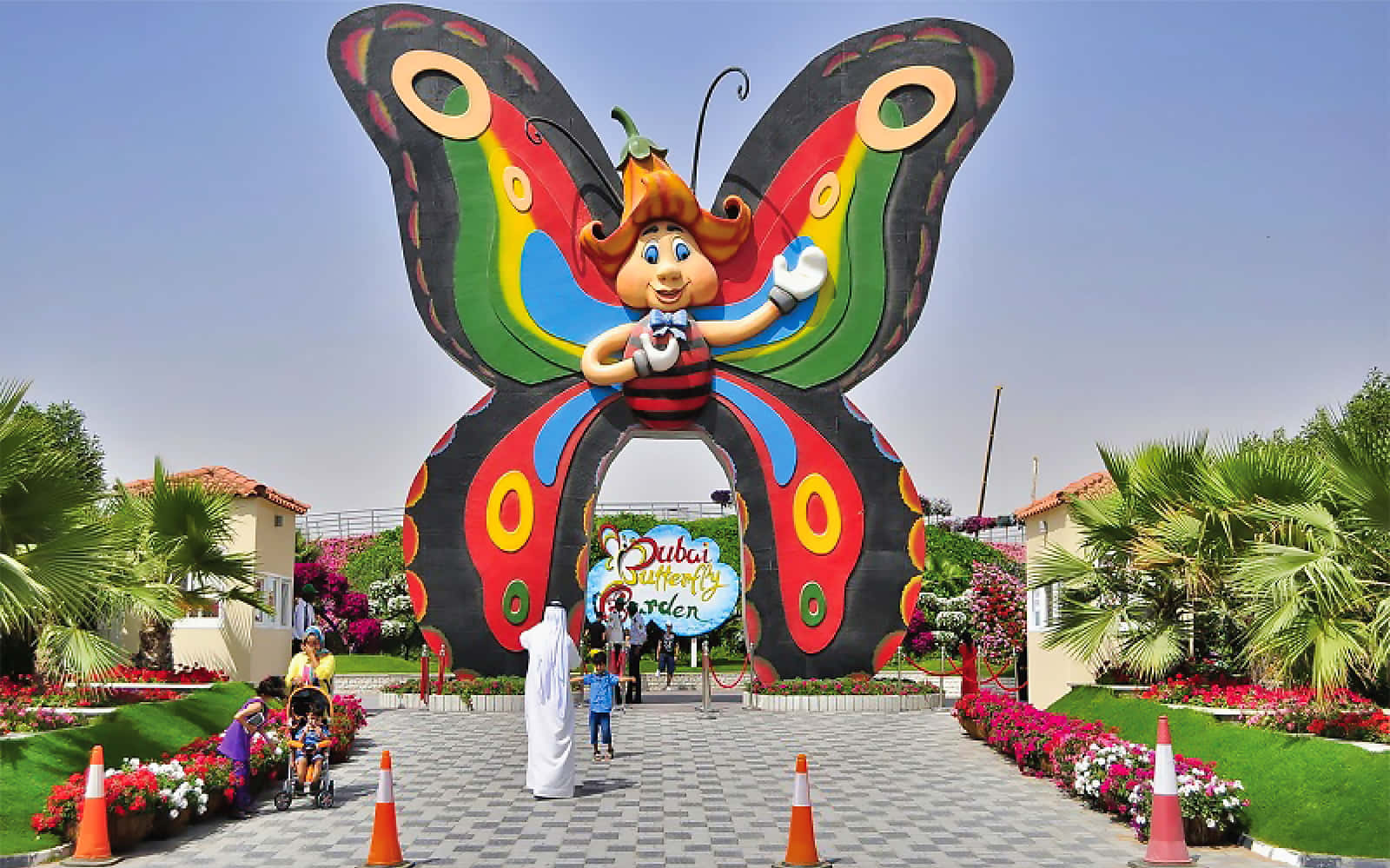 Butterfly Park 桌布 壁紙 — 一個巨大色彩繽紛的蝴蝶雕塑，帶有卡通人物，在晴朗的藍天下向進入杜拜蝴蝶花園的遊客揮手。